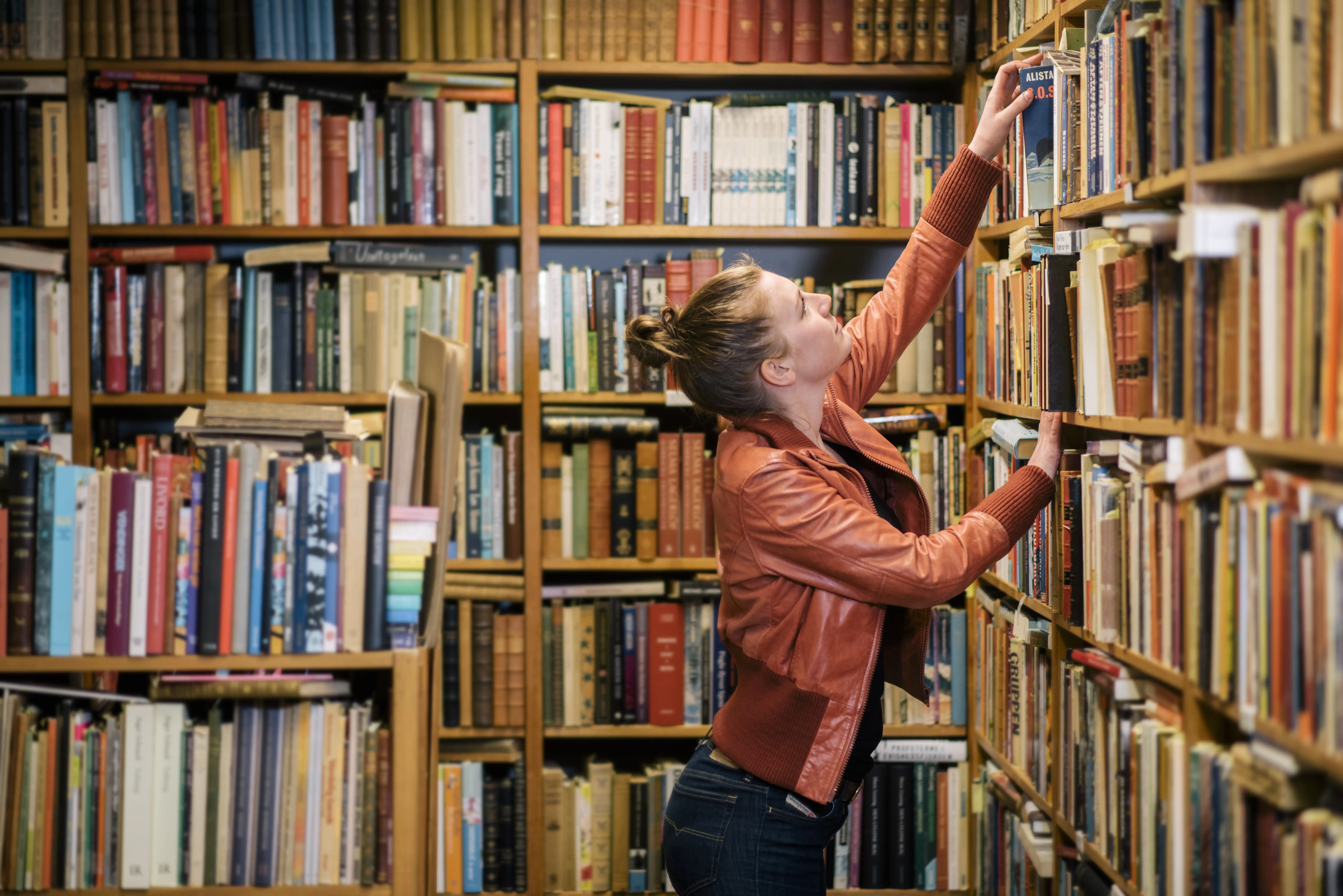 A woman reaching for a book on a shelf in a book shop