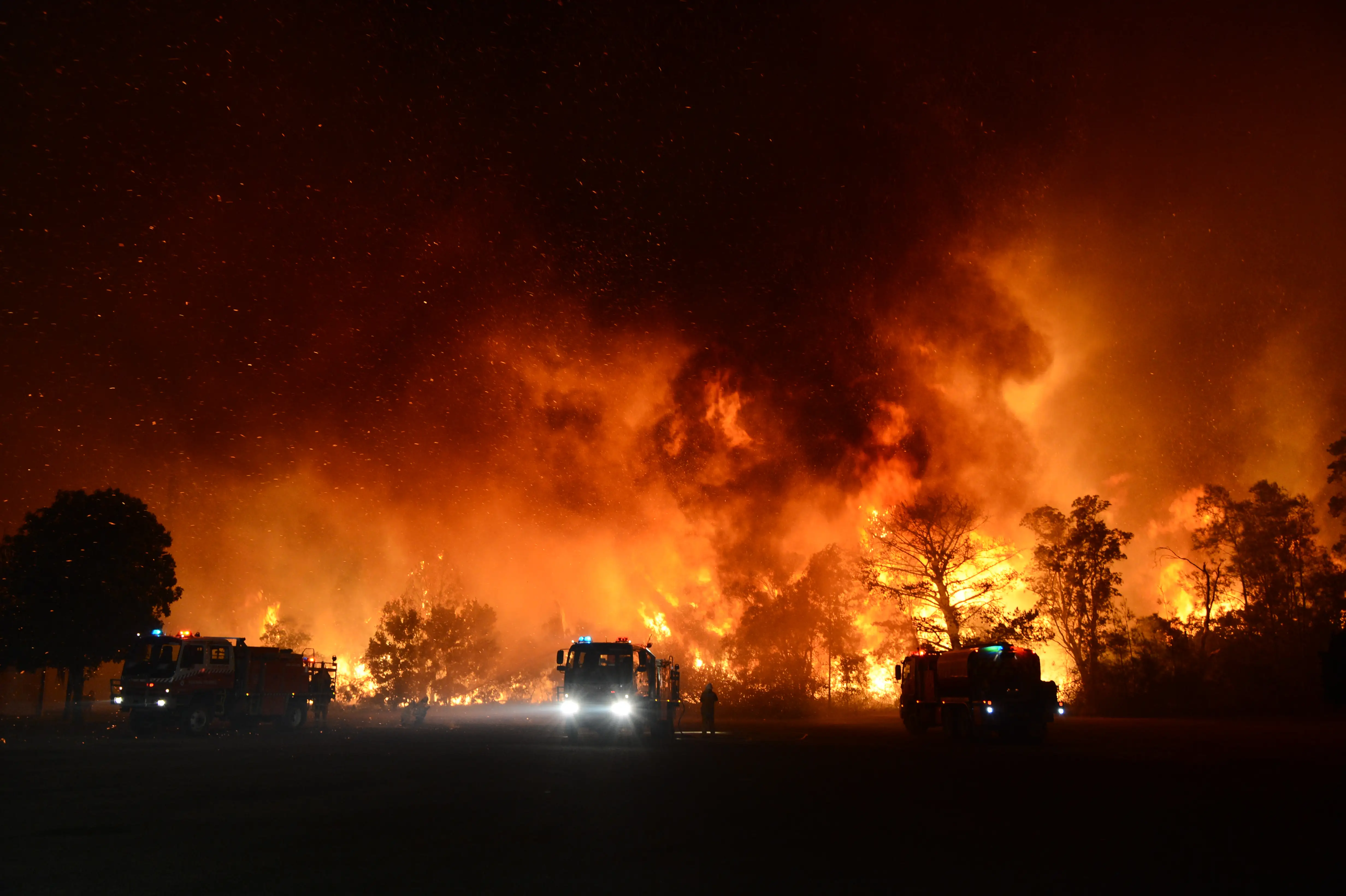 Firemen prepare as a bushfire approaches homes as smoke billows around them