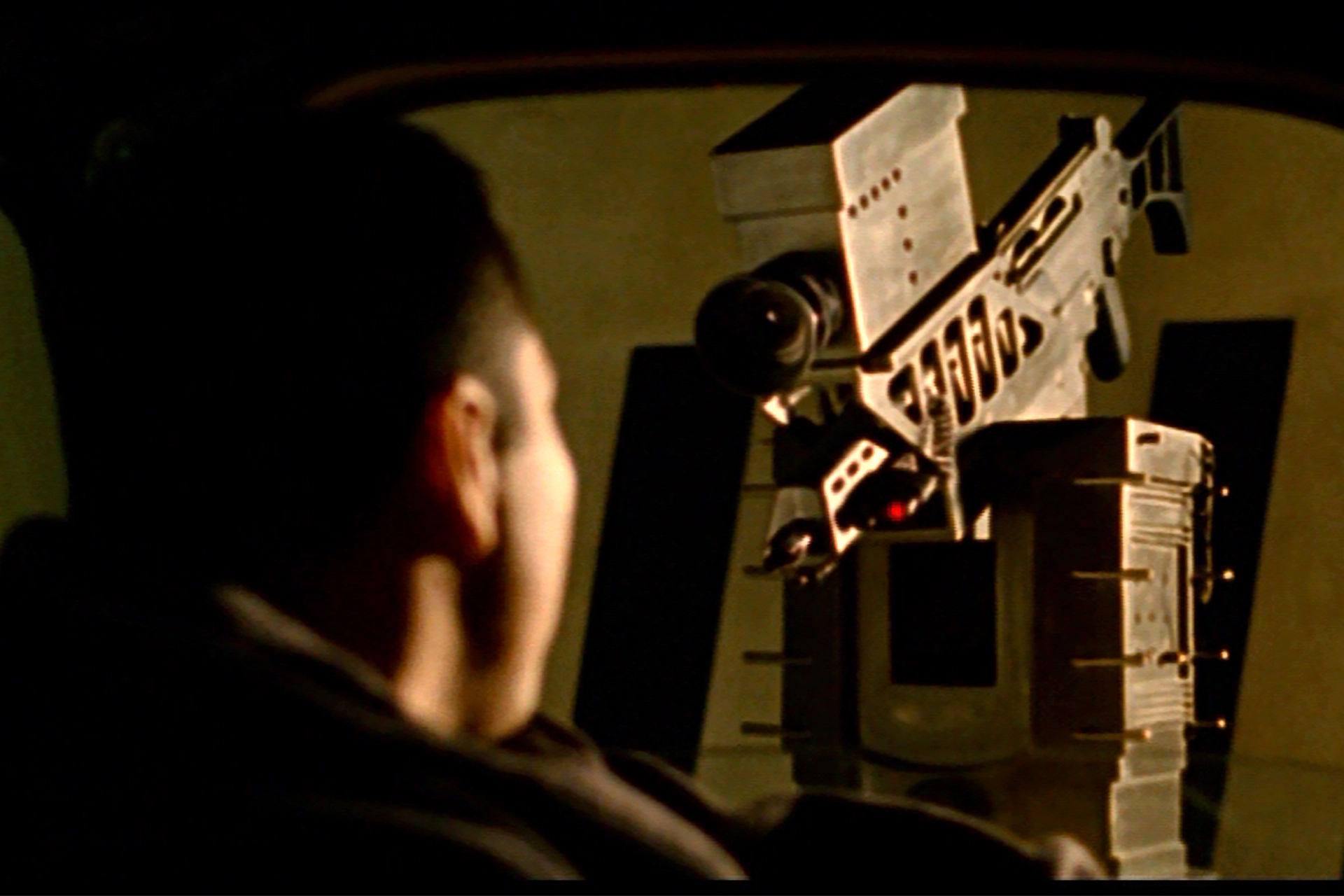 Still from Sleep Dealer film, showing a man sitting in a car having his iris scanned by an old-fashioned camera