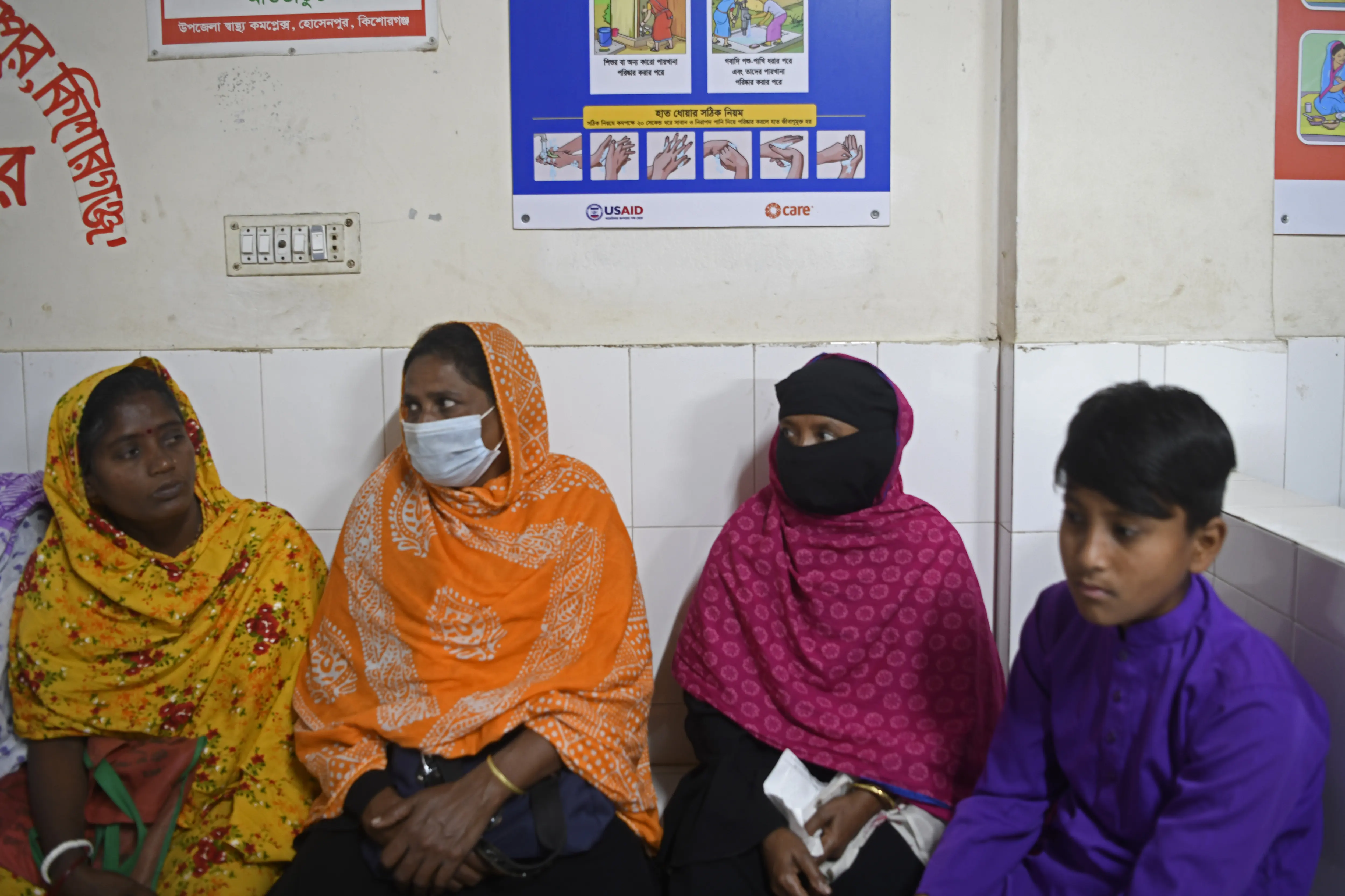 Women wait for treatment in Bangladesh with a USAID (U.S. Agency for International Development) banner visible in the background