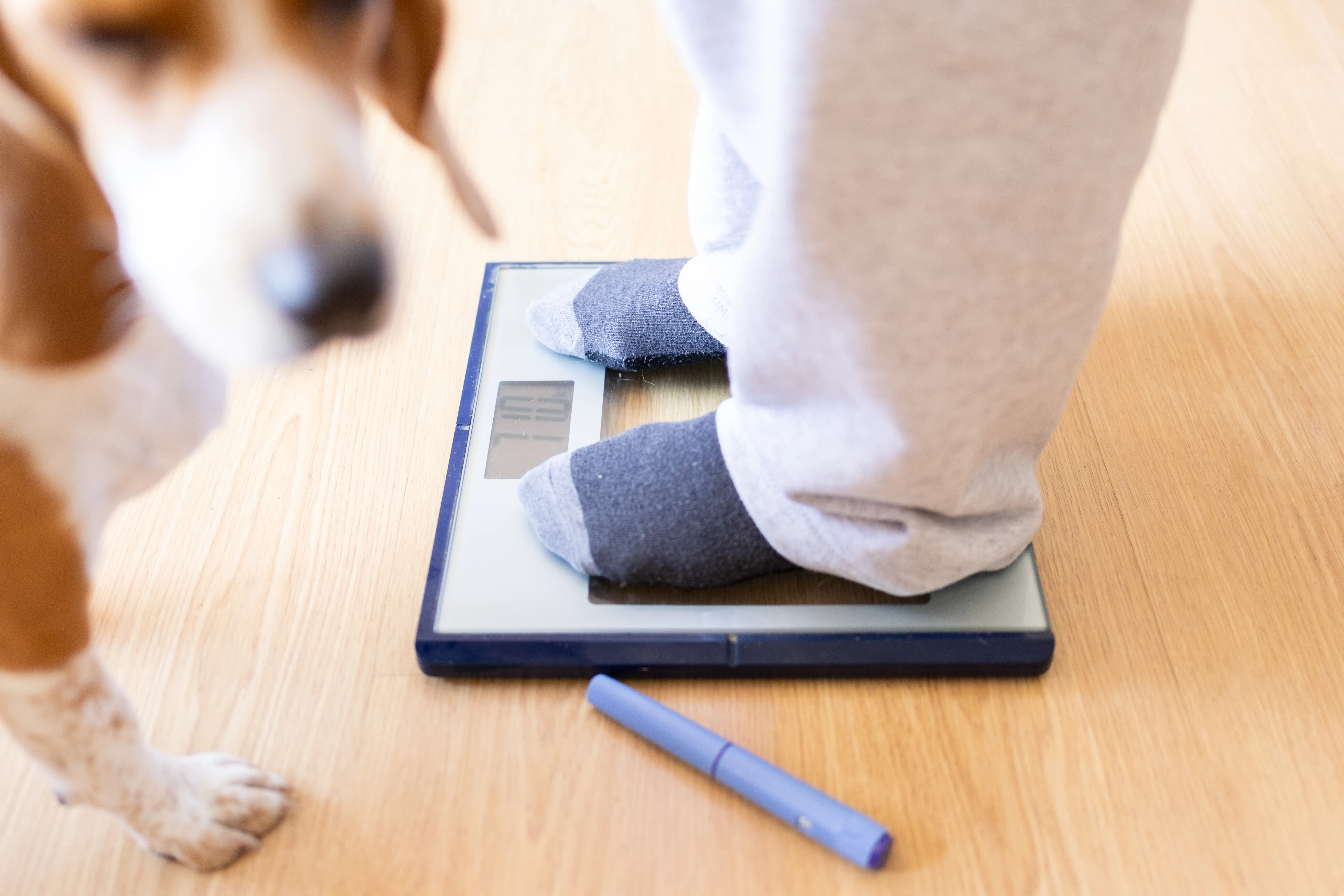 Woman checking her weight on a scale at home, with a semaglutide injection pen nearby.
