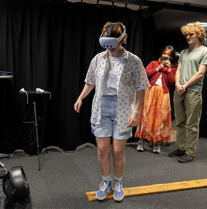 A person wearing a VR headset and walking on a plank that lies on the ground