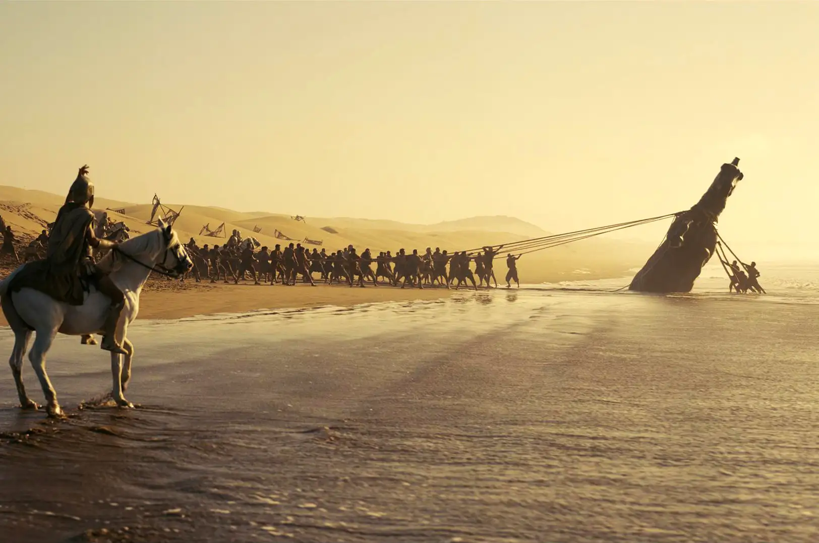 A distant shot of a crowd of soldiers pushing a boat out into the ocean from a beach
