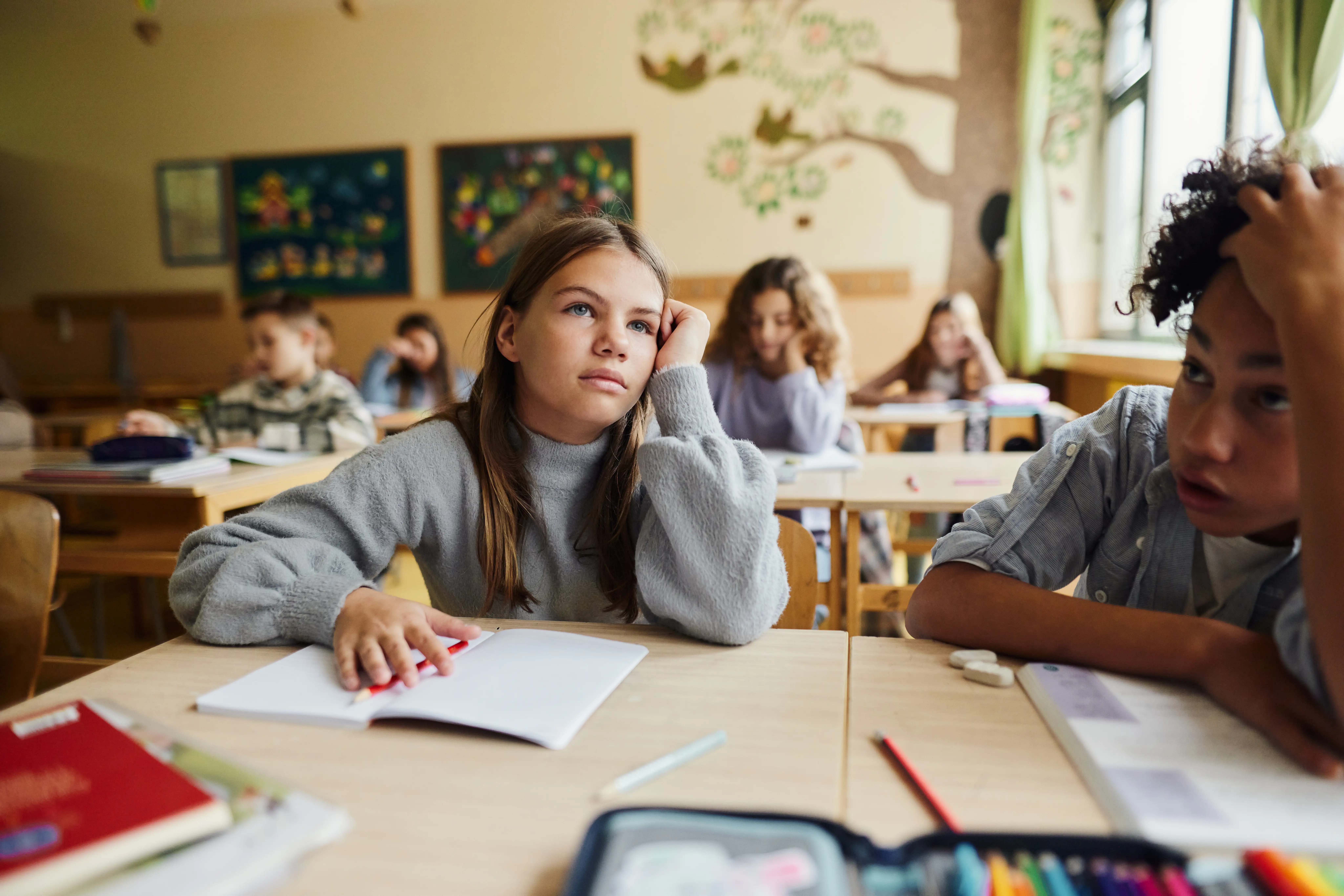A girl in a classroom looking thoughtful while her classmates work