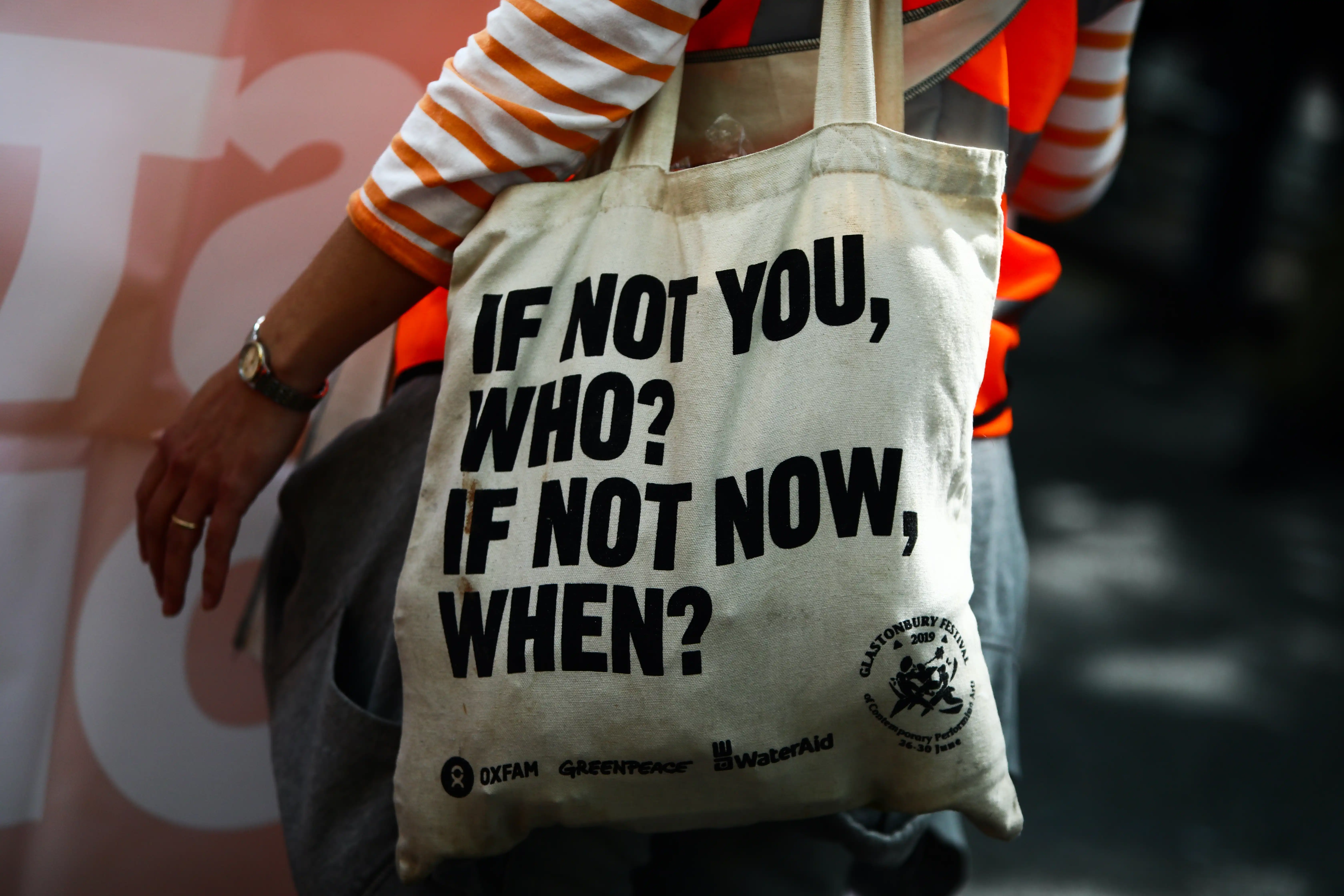 A person at a rally wears a tote bag that reads ‘If not you, who? If not now, when?’