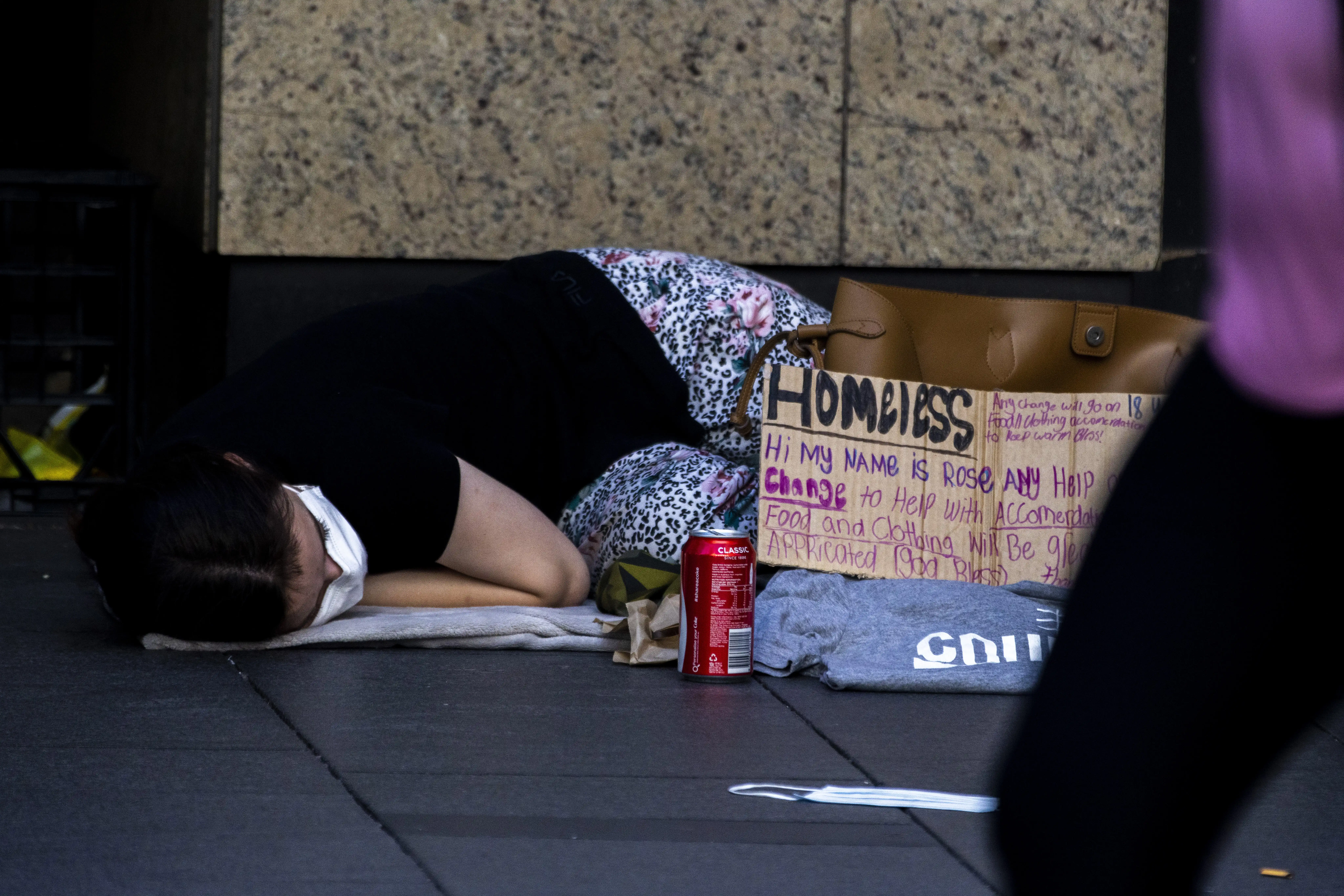 A person sleeping rough in Sydney with a cardboard sign asking for help