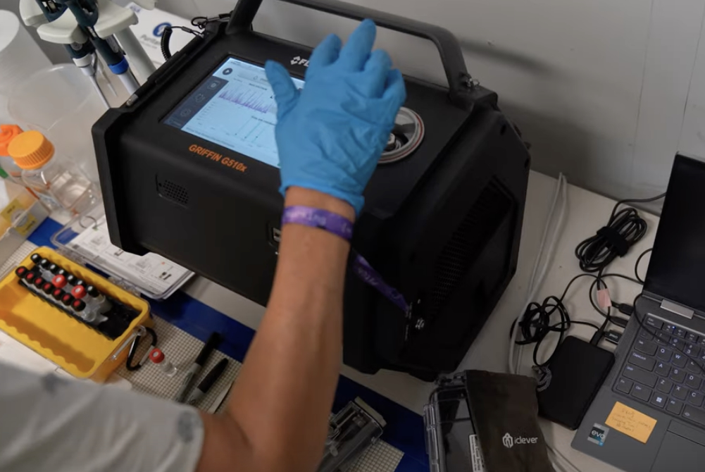 A gloved health worker putting details into a Gas Chromatography Mass Spectrometry machine