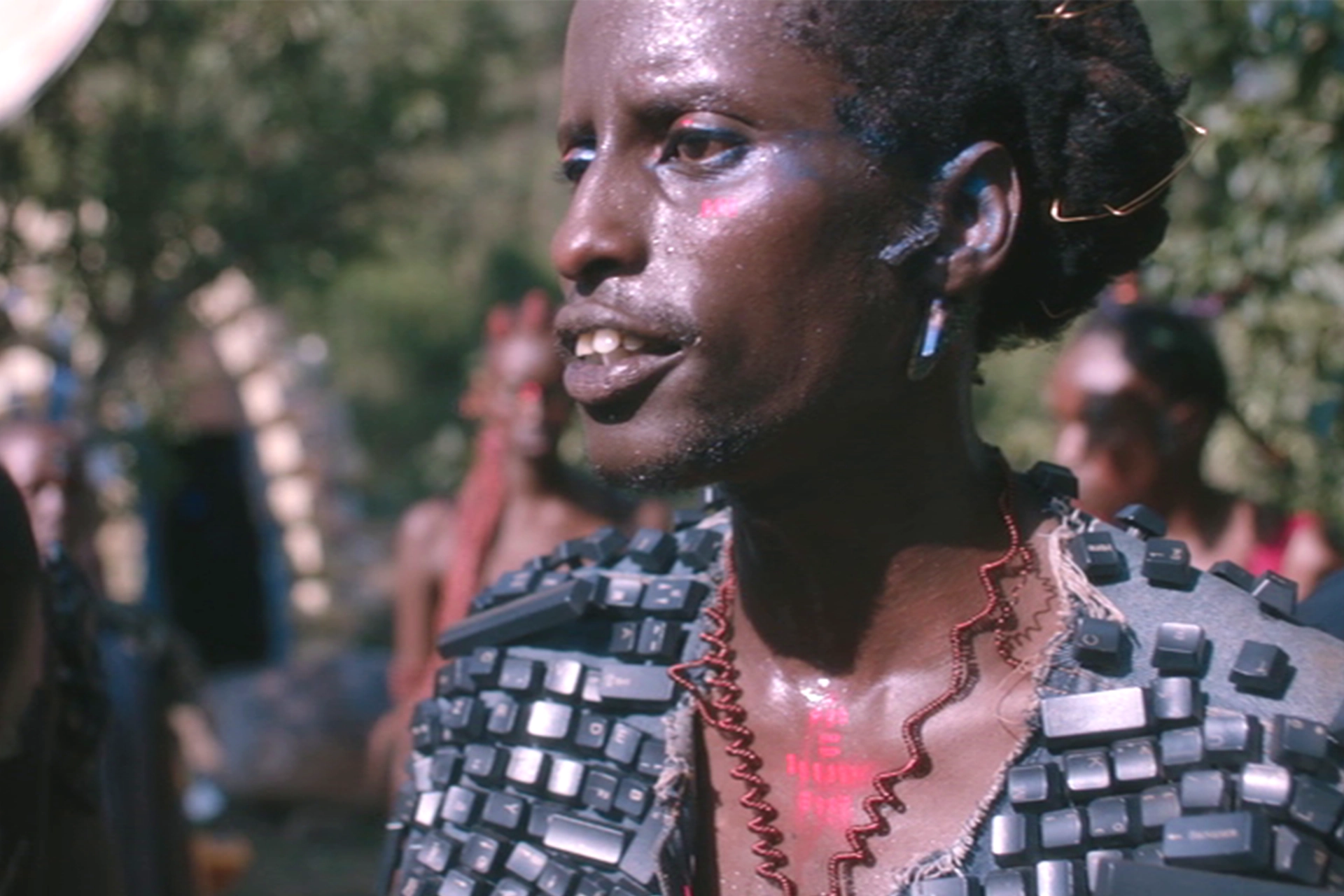 Still from Neptune Frost film, showing an African woman wearing a jacket made from old computer keyboard letters