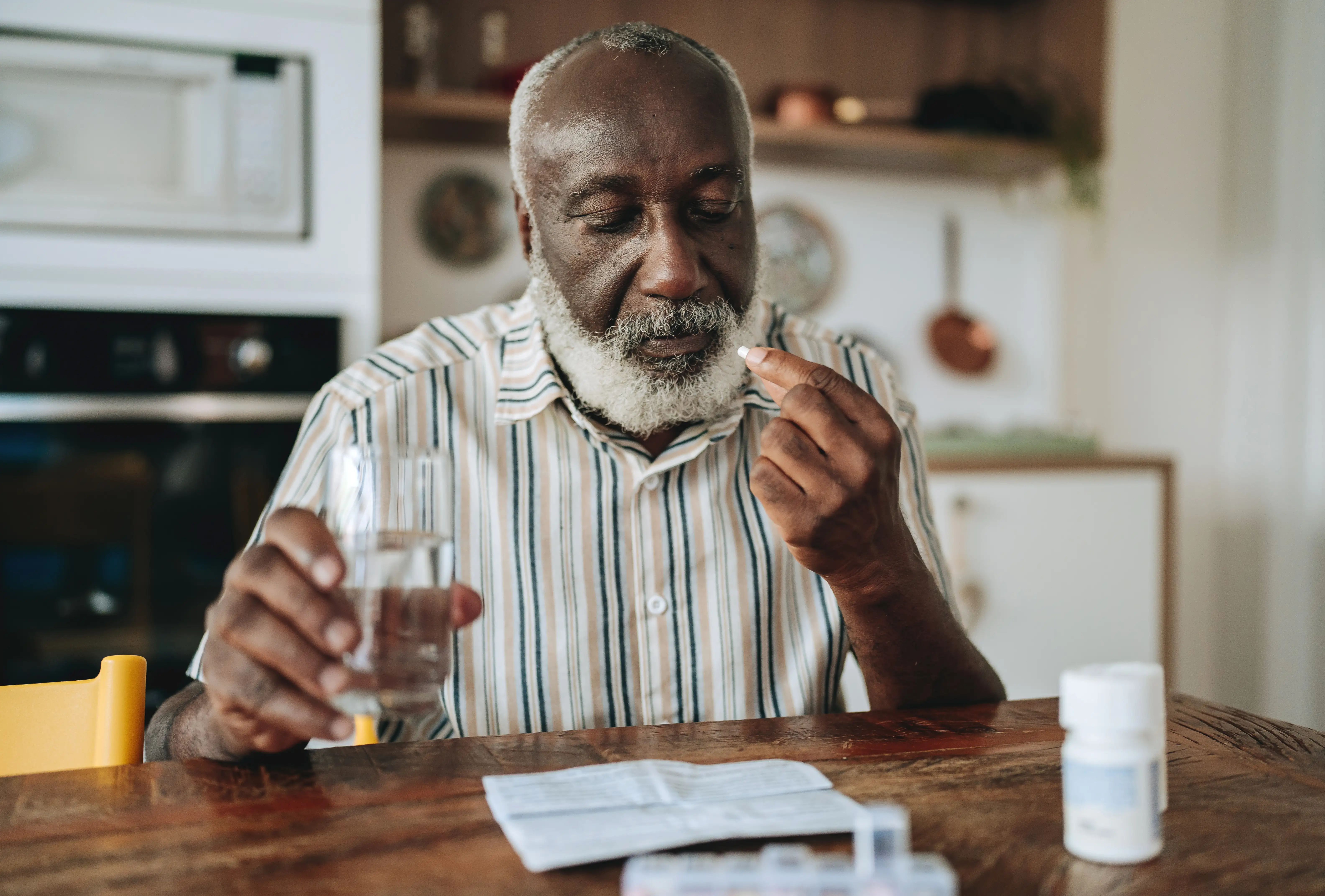 A senior man taking antibiotics in the kitchen at home