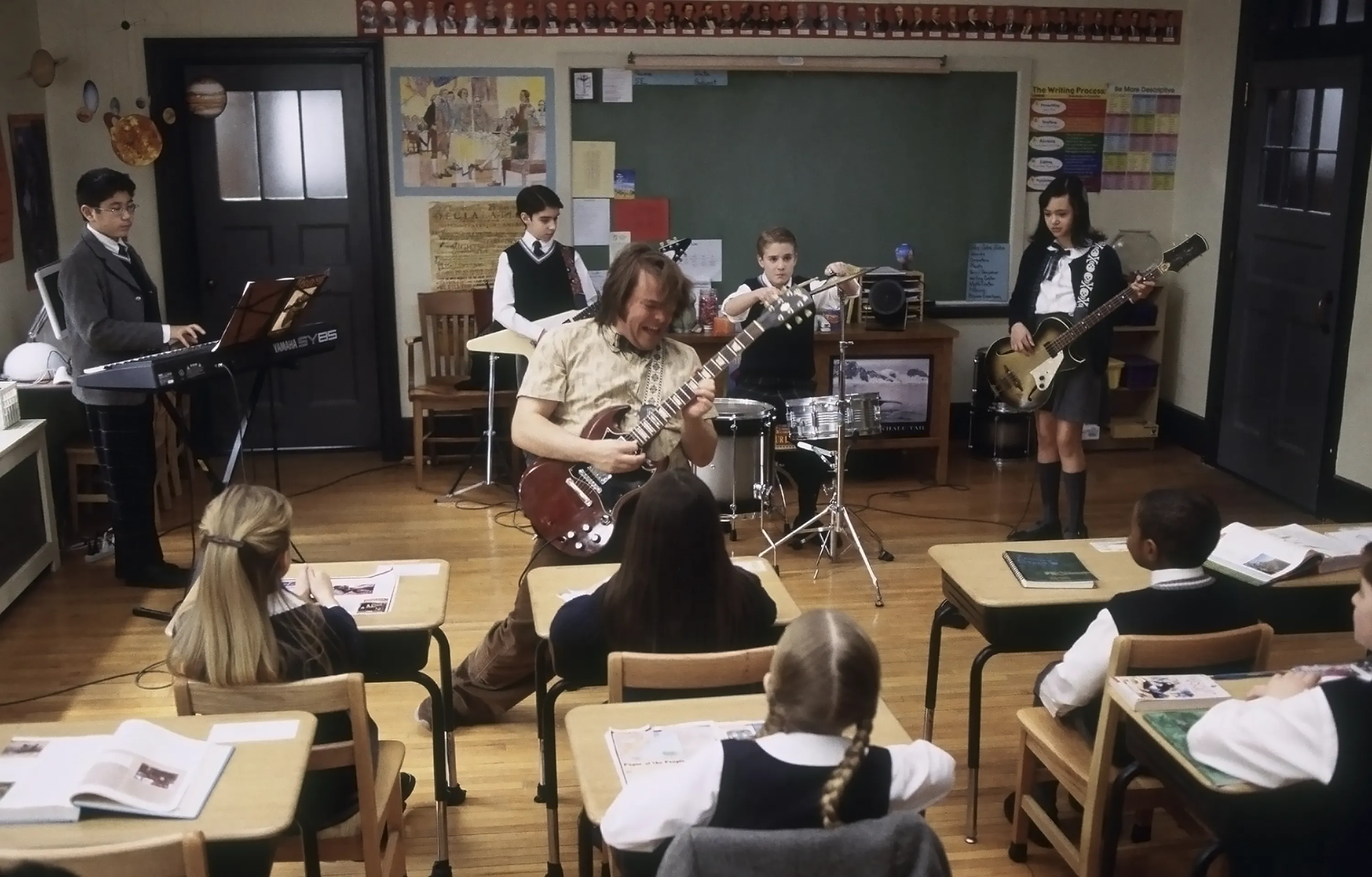 A still from the School of Rock showing Mr Schneebly playing guitar in front of a class