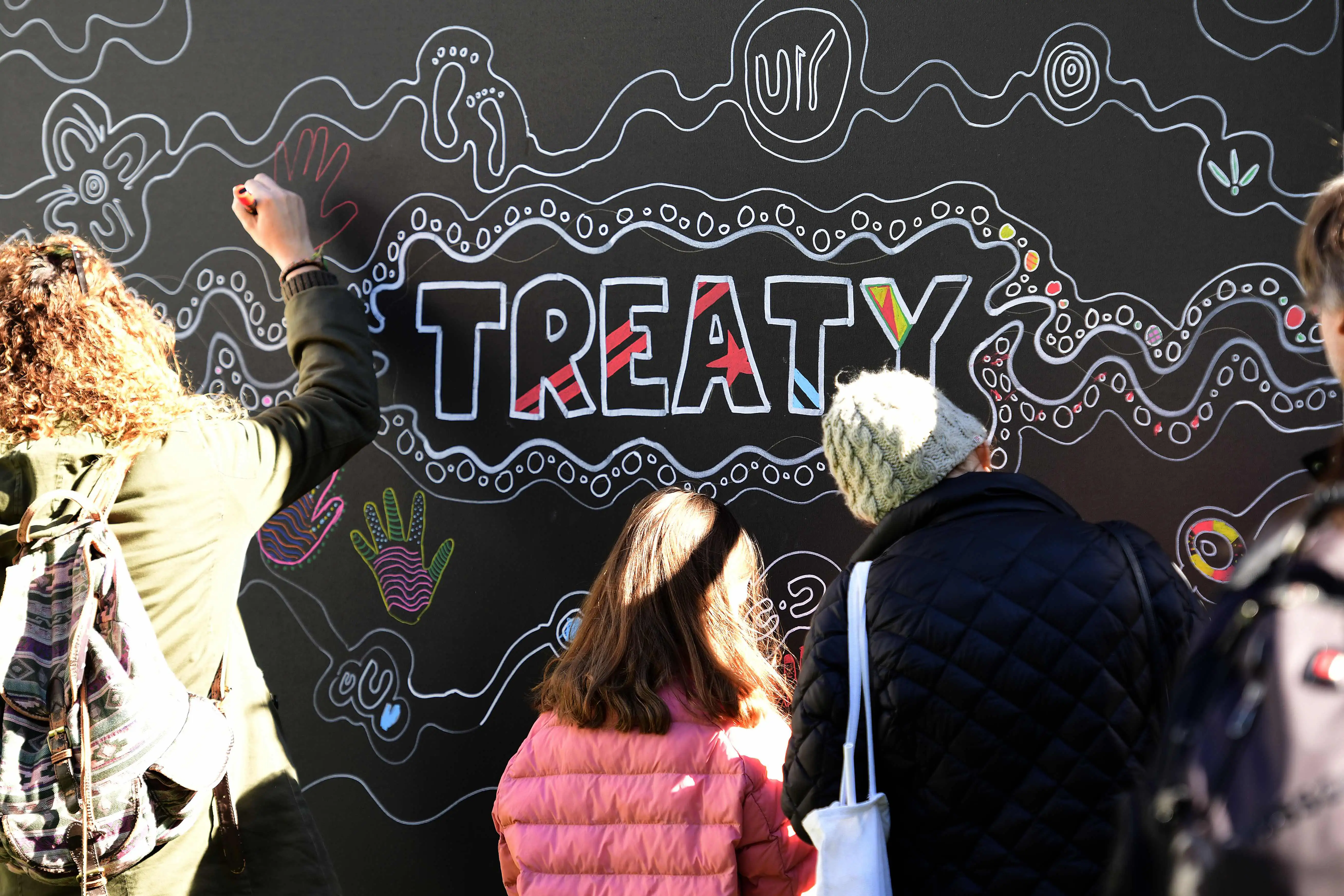 People drawing on a communal artwork around the word ‘treaty’.