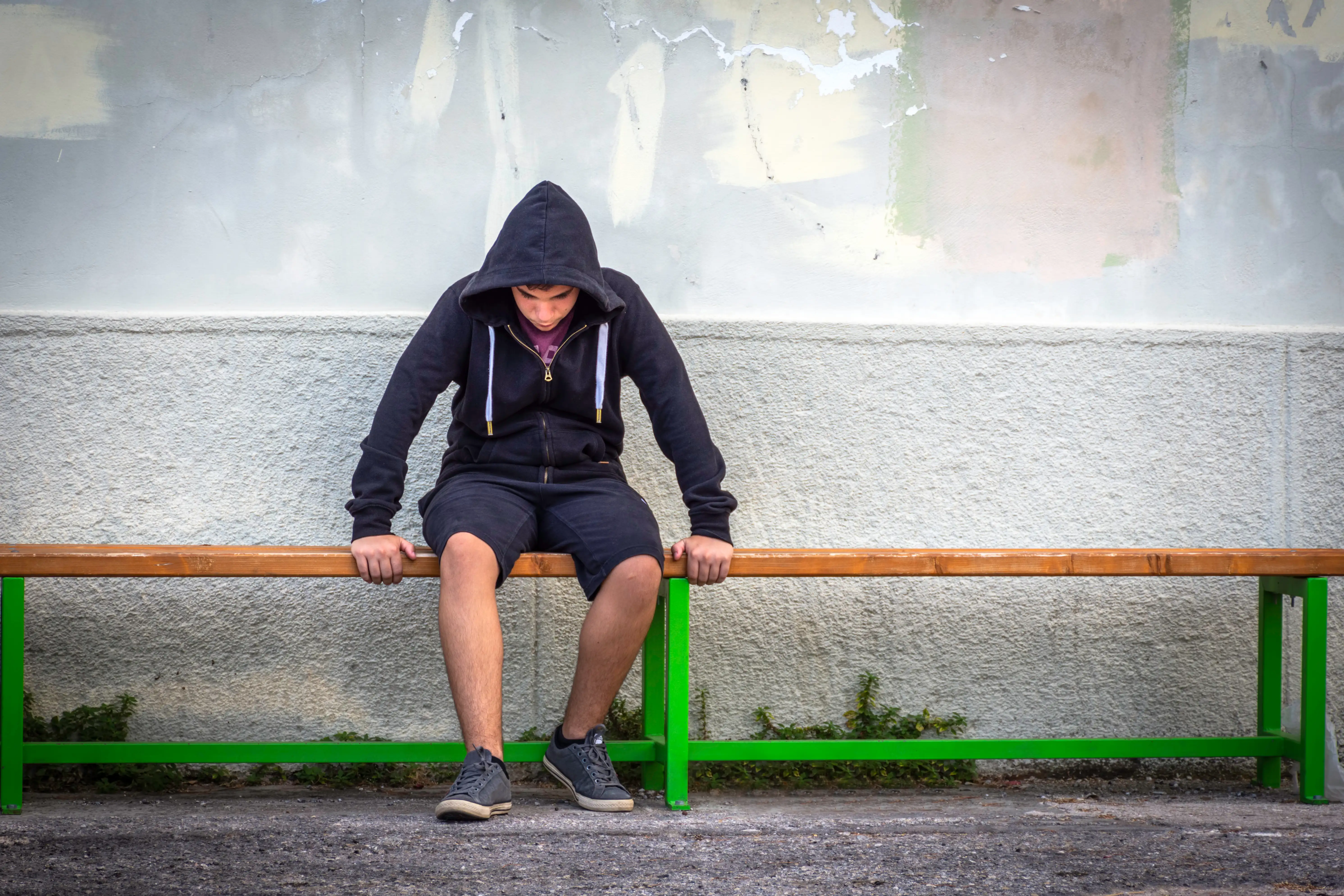 A teenage boy sitting alone looking stressed at a bus stop