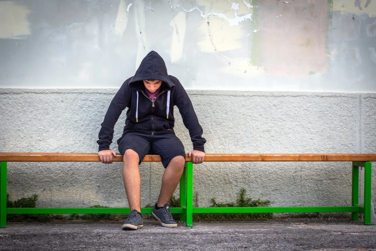 A teenage boy sitting alone looking stressed at a bus stop