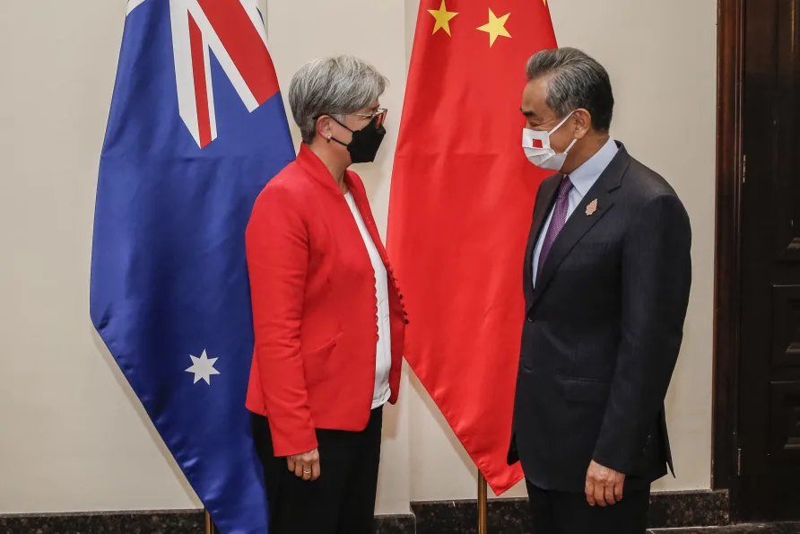 A man and women wearing face masks standing facing each other with the Australian and Chinese flags in the background