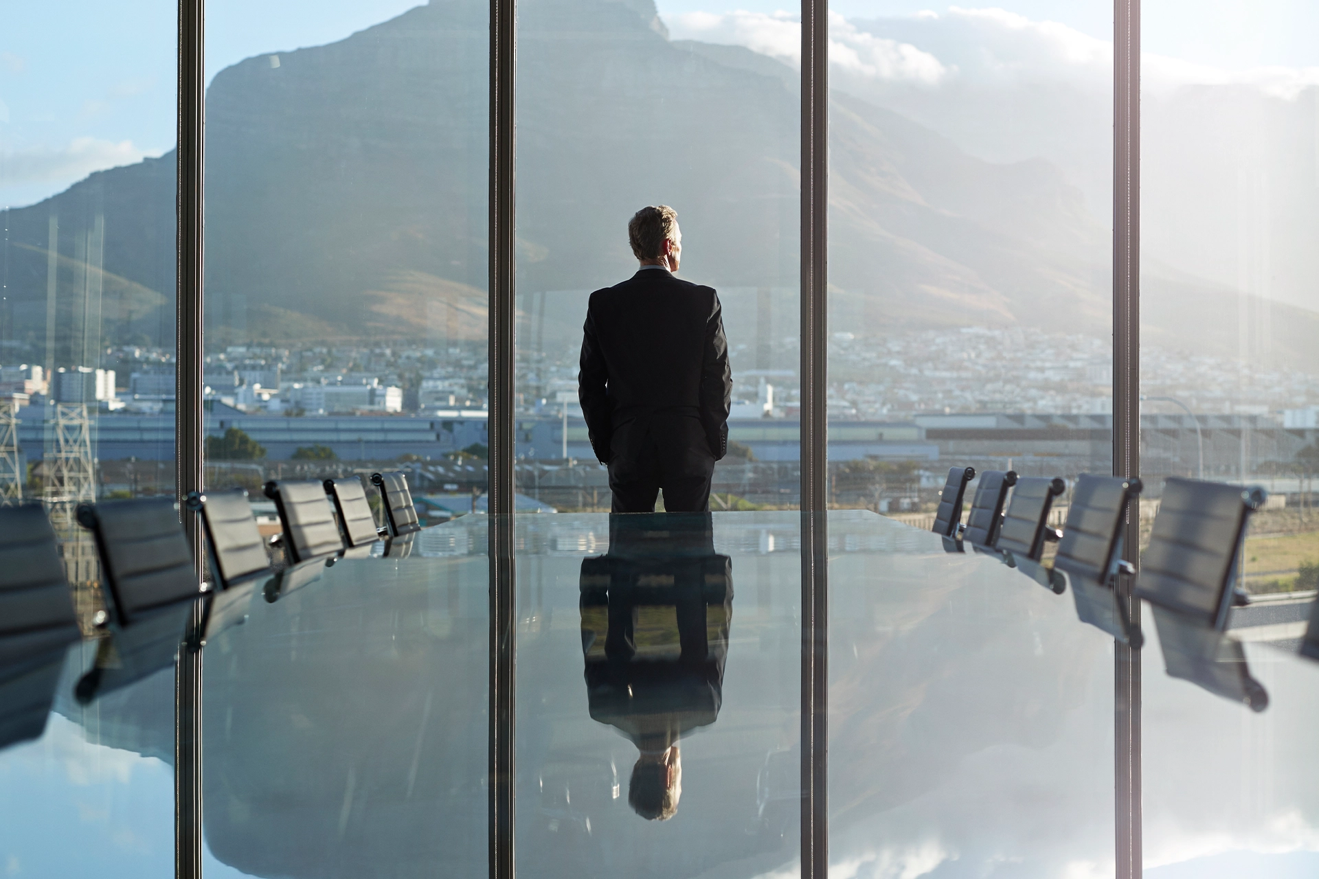 Businessman standing in large office, looking out a window with his back to the room