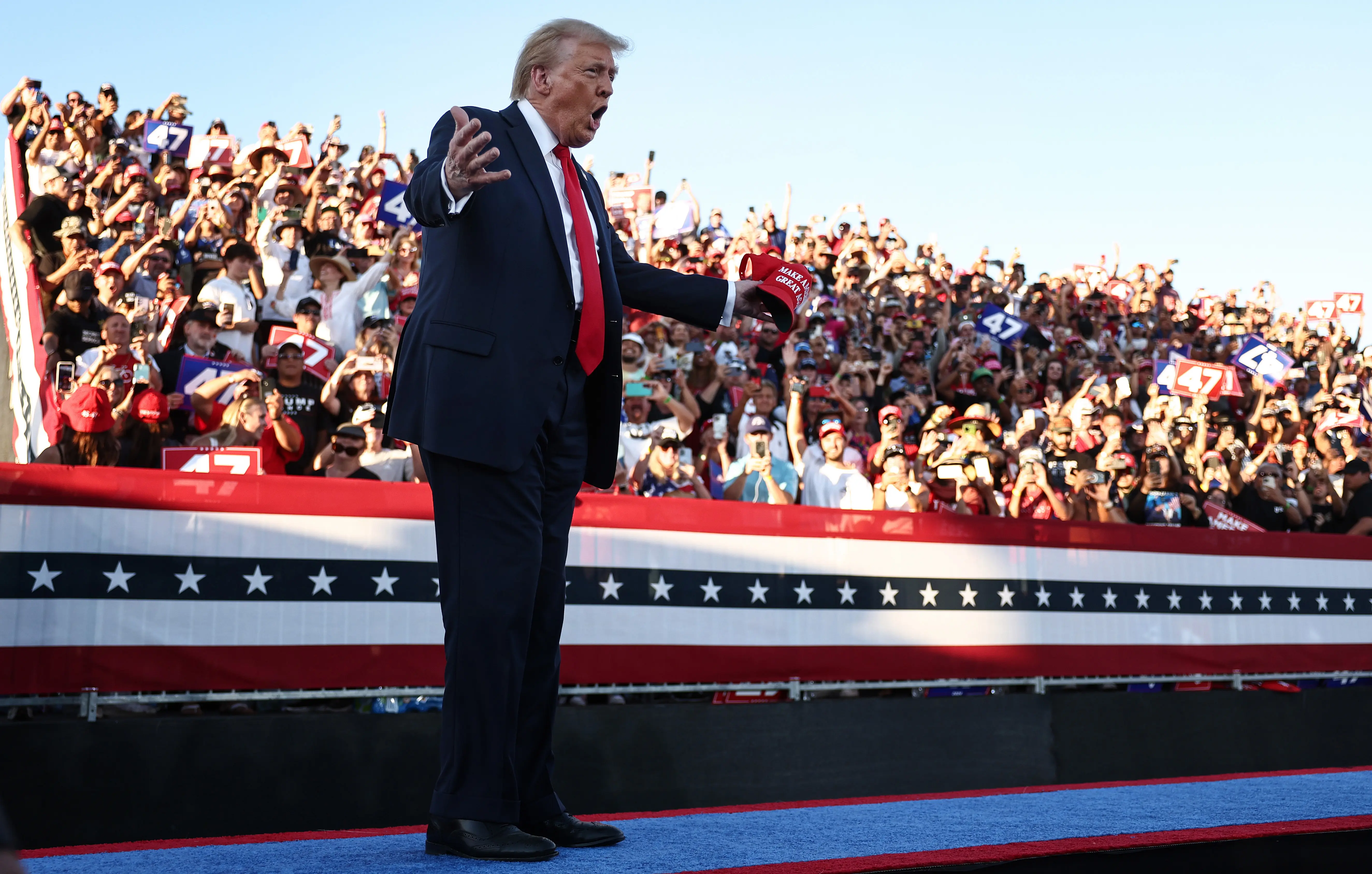 Donald Trump on stage shouting as supporters raise their arms.