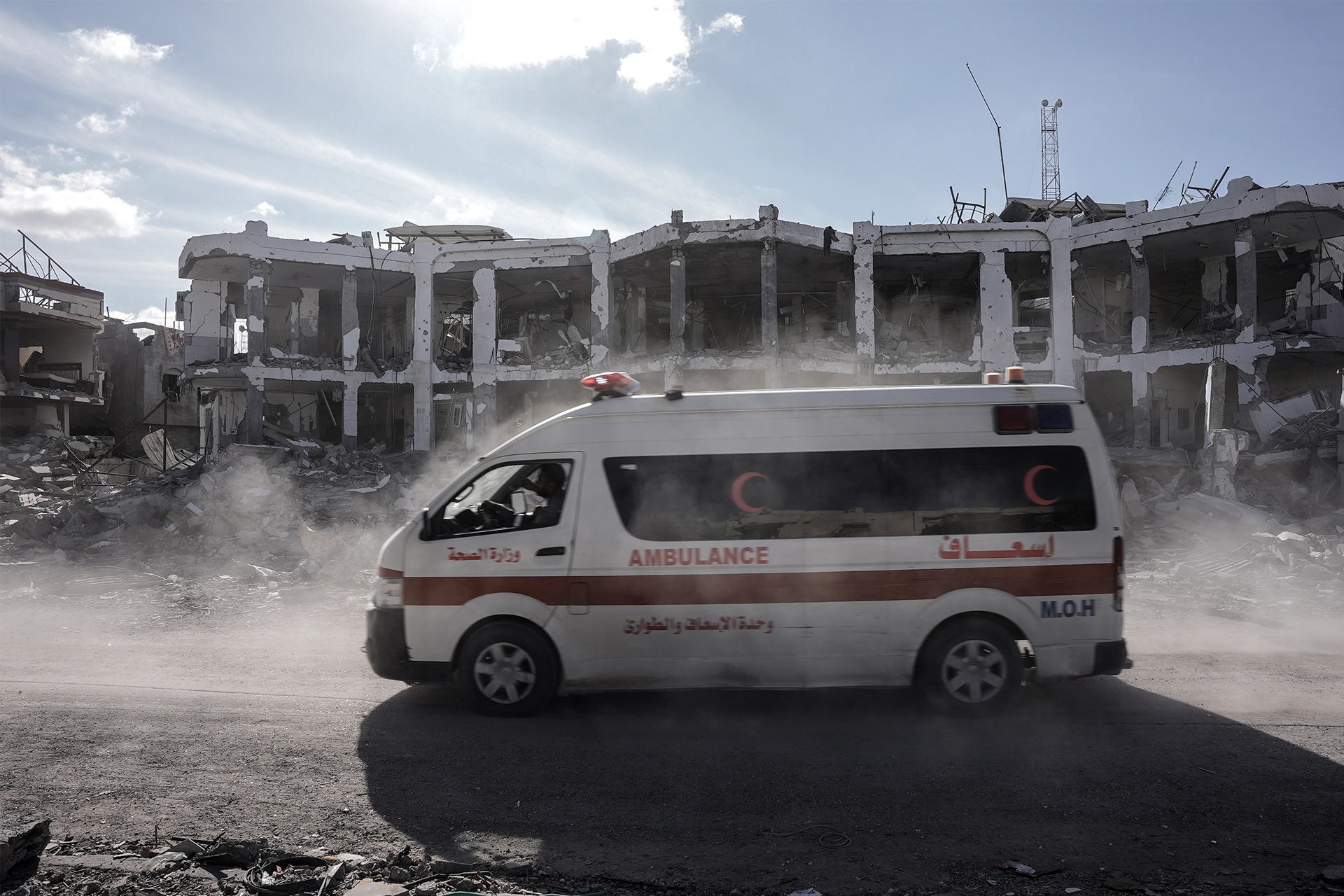 Ambulance in Gaza driving past a badly bombed hospital building