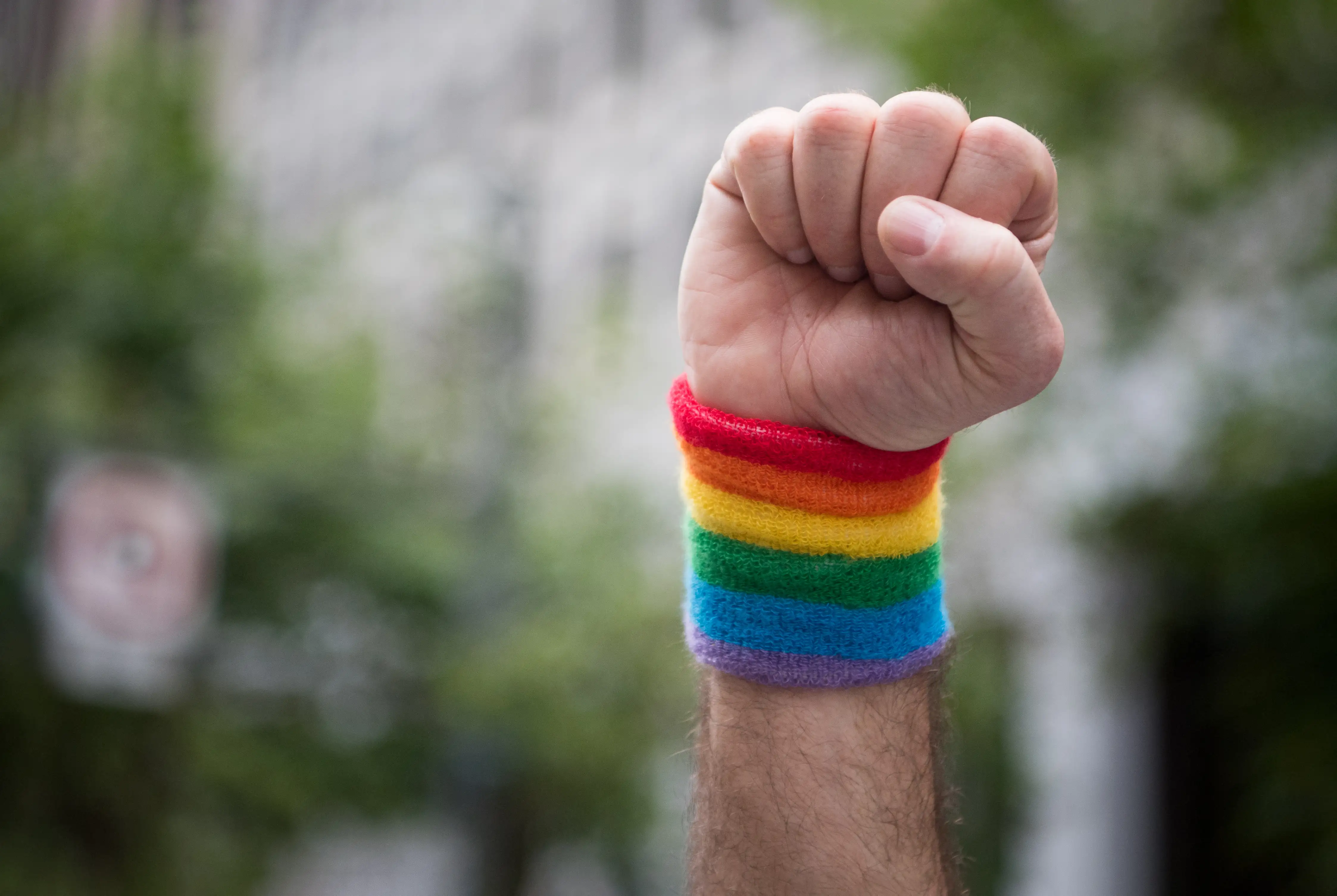 A man raises his fist wearing a rainbow wristband while marching in the Pride parade
