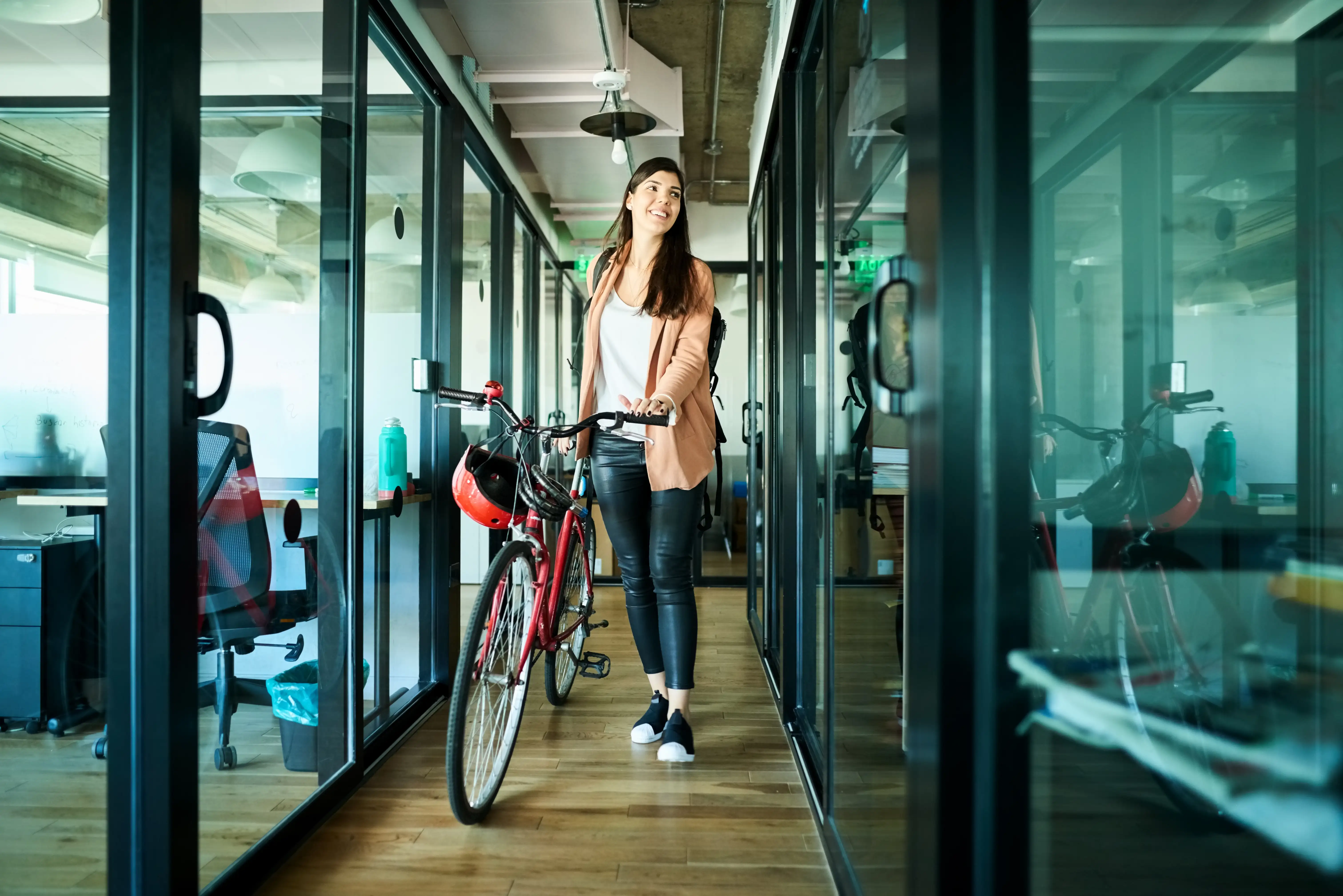 Young businesswoman pushing her bicycle out of the office