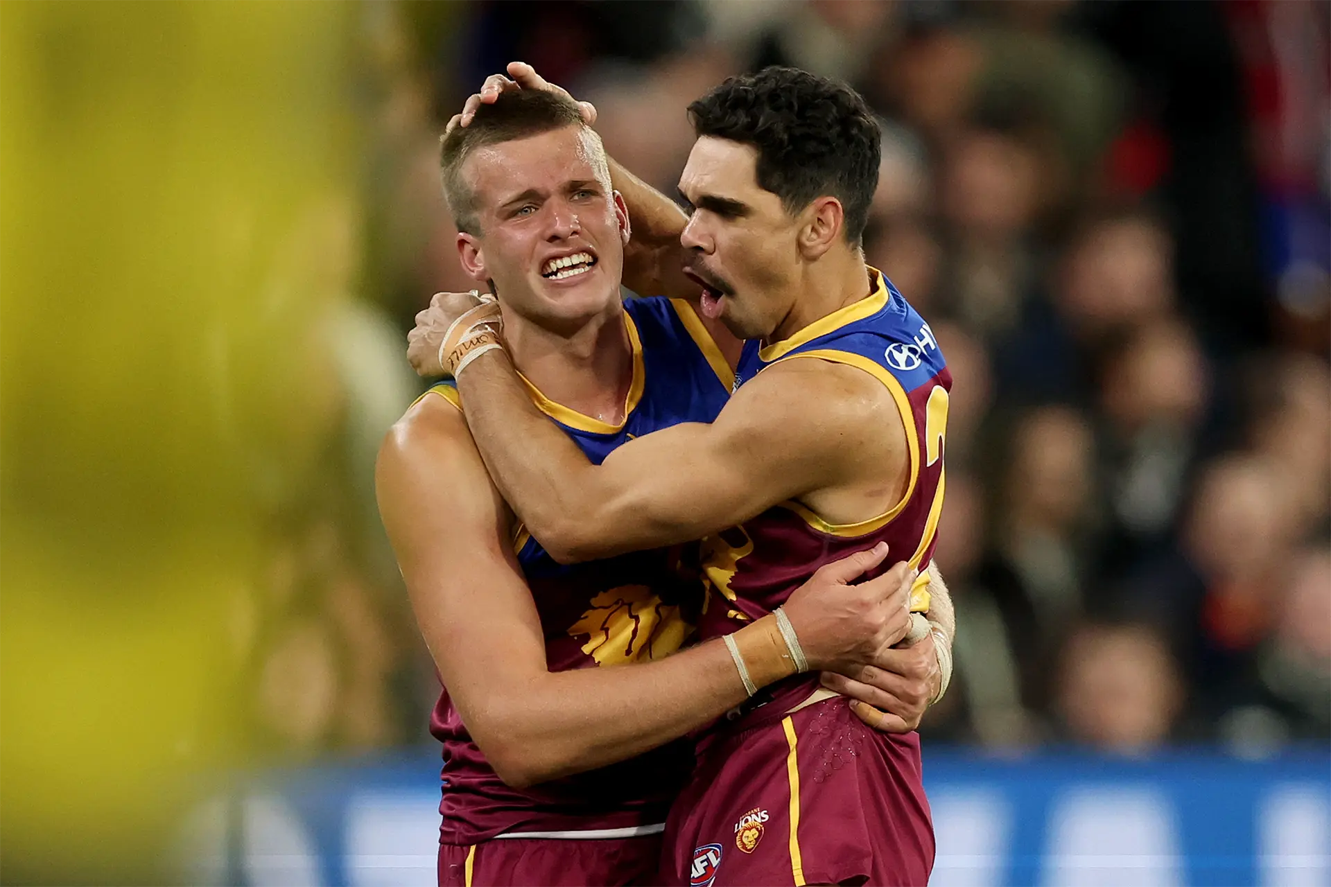 Two Brisbane Lions AFL players embracing in celebration on the football field