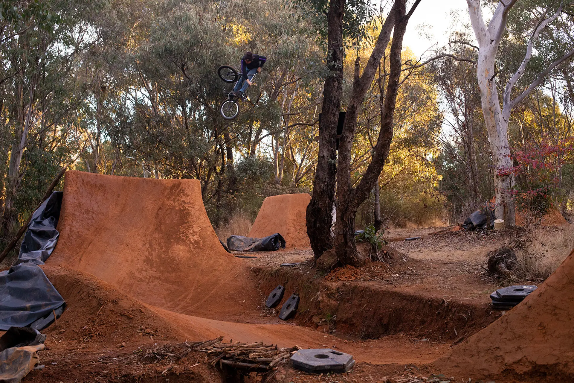 A man on a BMX in mid-jump off in a dirt jumps track