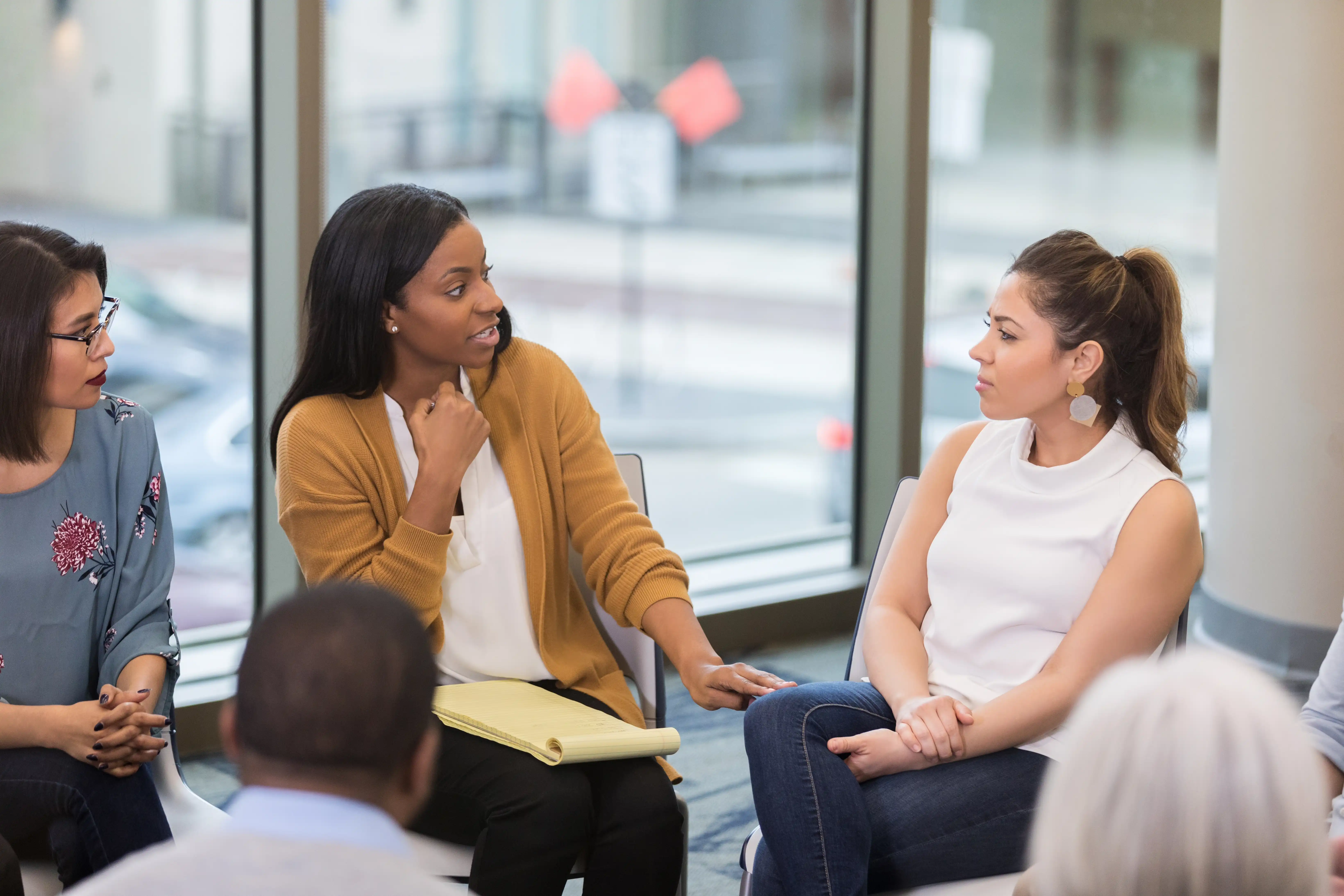 A women in a yellow cardigan gestures with her hands as she speaks to another woman in a group training session