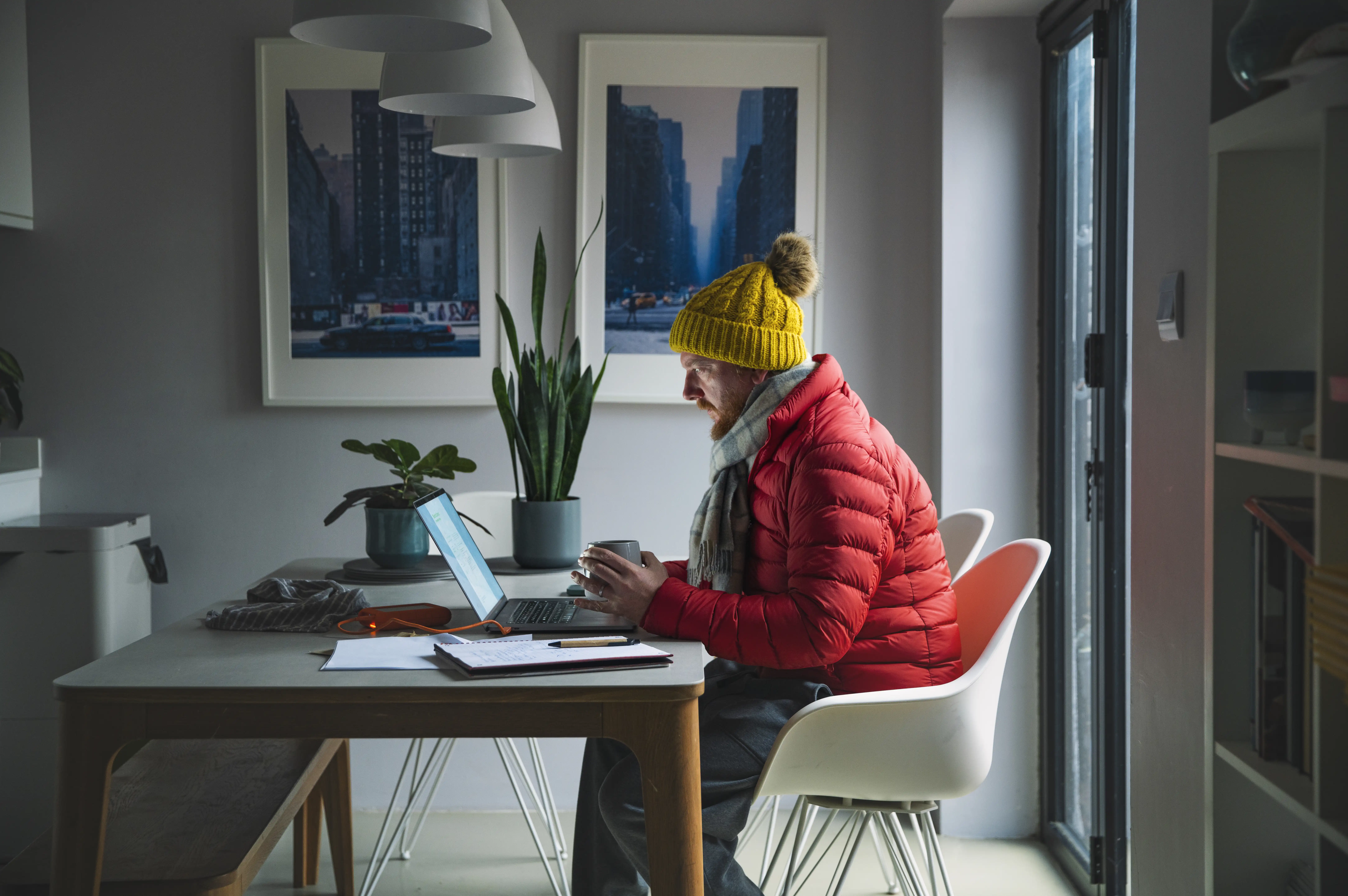 A man working at home weather a big winter jacket and beanie