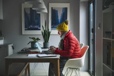 A man working at home weather a big winter jacket and beanie