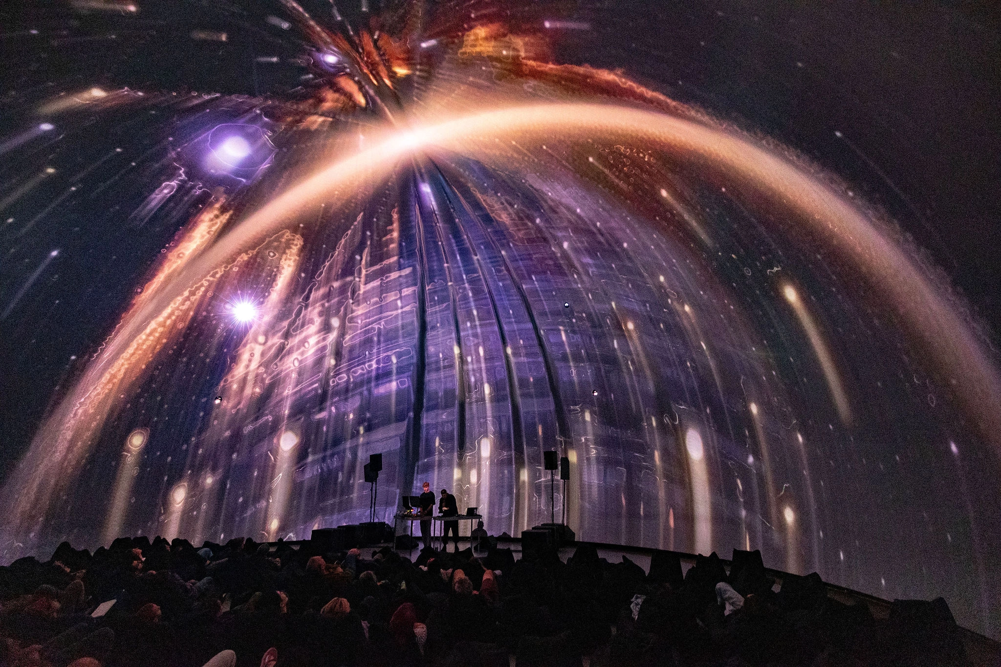 A spherical screen in a planetarium style venue displays dancing lights
