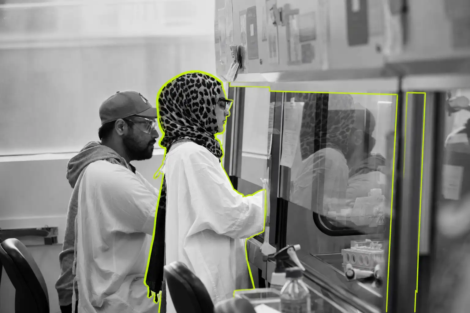 A black-and-white photo of two researchers working in a medical lab with elements picked out in lime green