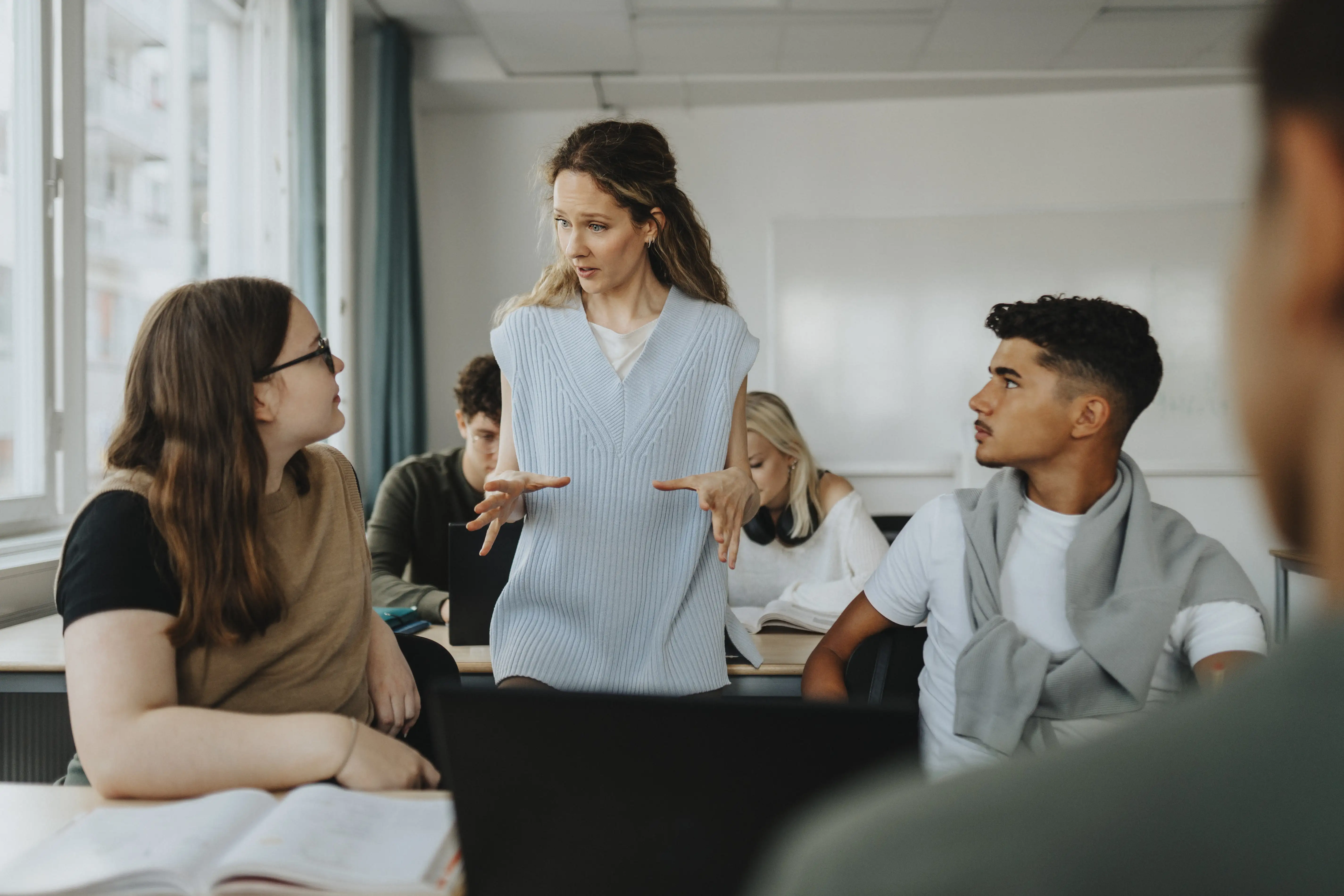 Female teacher gesturing while explaining to teenage boy and girl in classroom