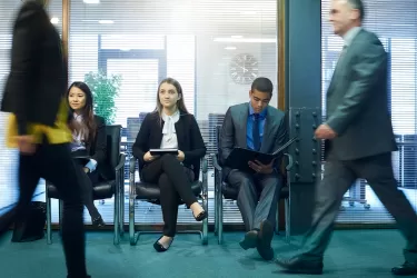 Office with business people walking and sitting waiting for a job interview