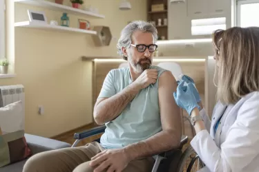 Disabled Male Patient Sitting in the Wheelchair Getting Vaccinated at His Home by Female Doctor