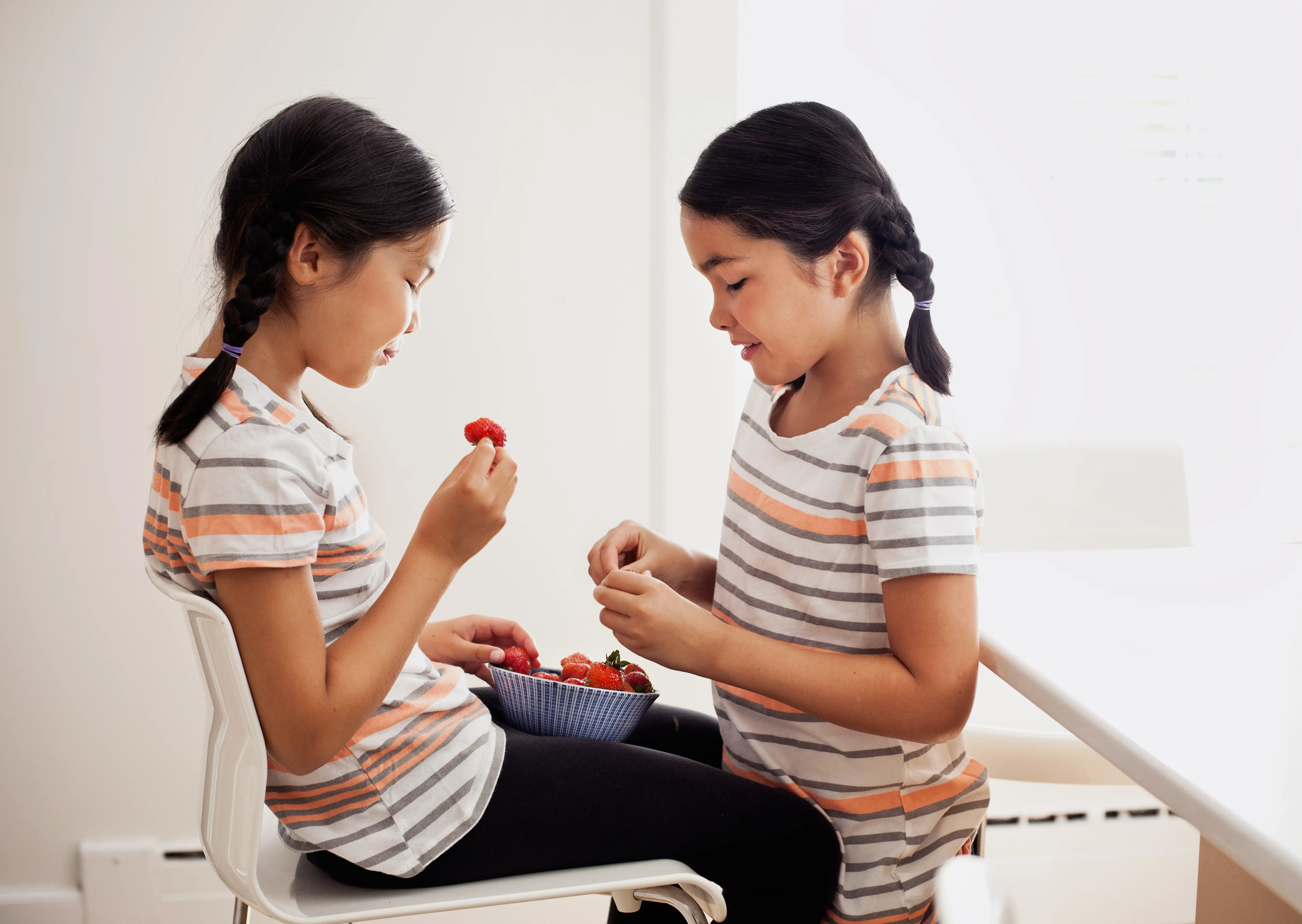 Young twins in striped shirts sharing strawberries