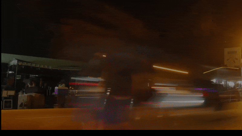 Cars and people move through a street in Ghana at night