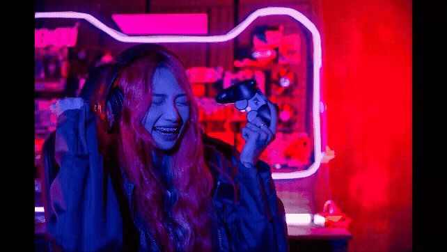 A young woman gamer celebrating a win with a console in her hand.