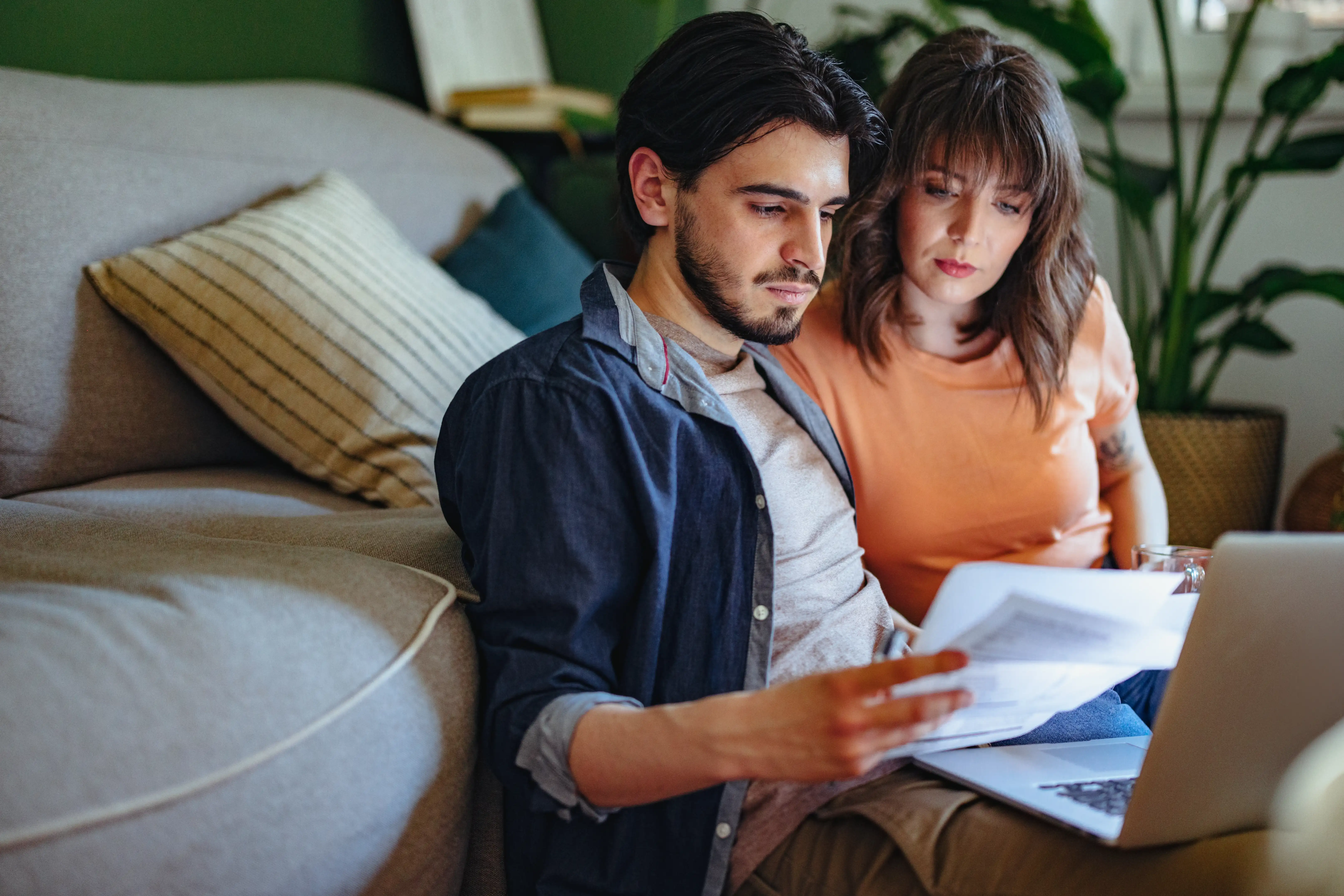 A man and woman sitting on a couch stare at a handful of household bills