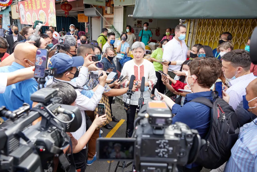 A woman speaking to many cameras and journalists on a street in Asia