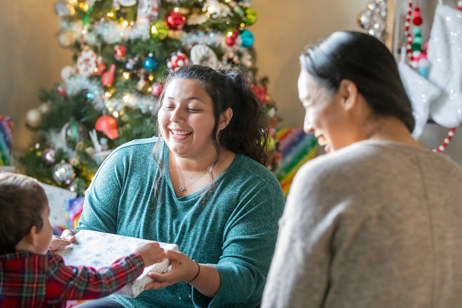 Two women smiling and giving Christmas gift to young son at home