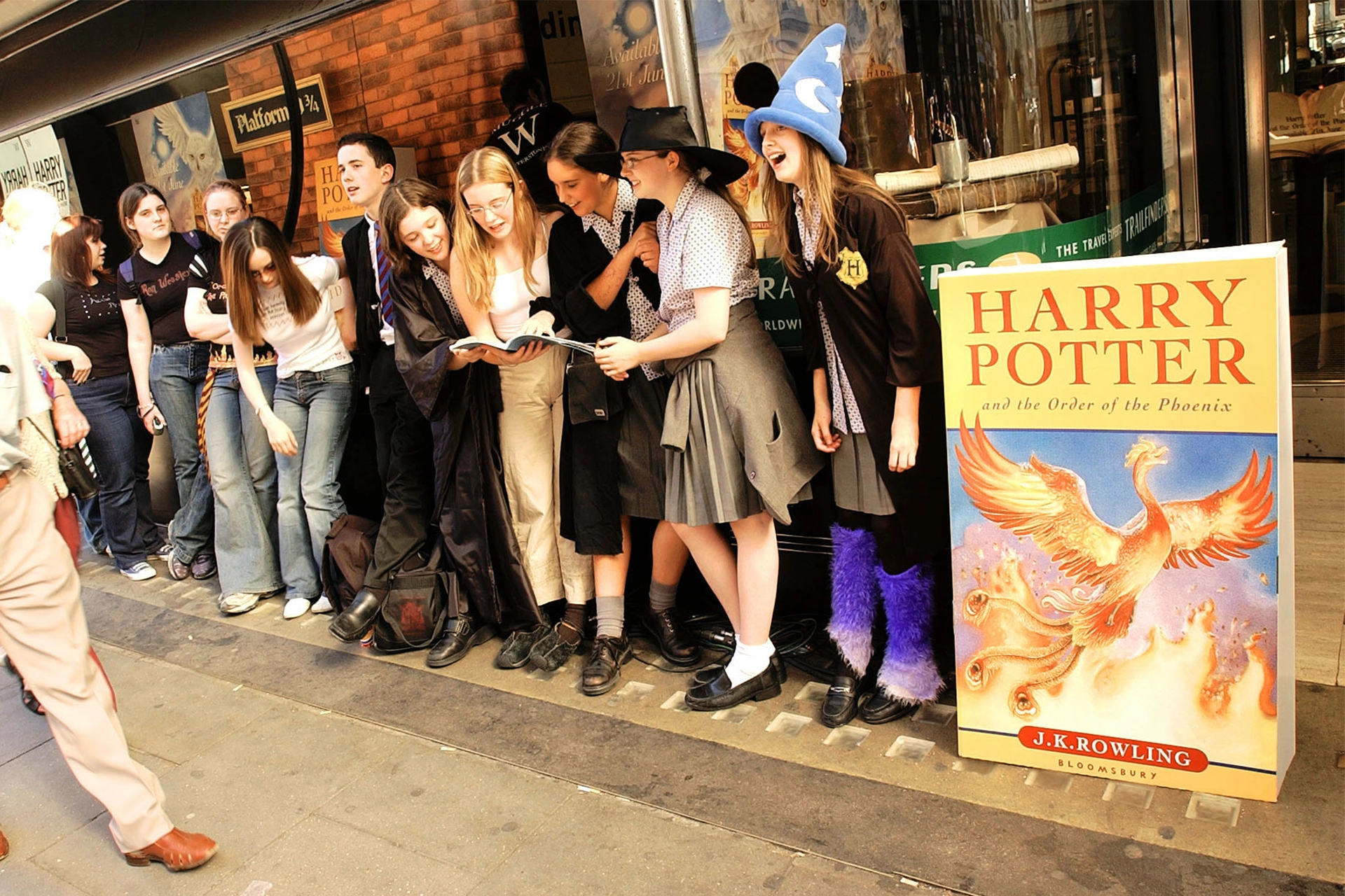 Lineup of teenage girls dressed as witches and wizards at launch of Harry Potter book. They stand next to an oversized version of Harry Potter and the Order of the Pheonix