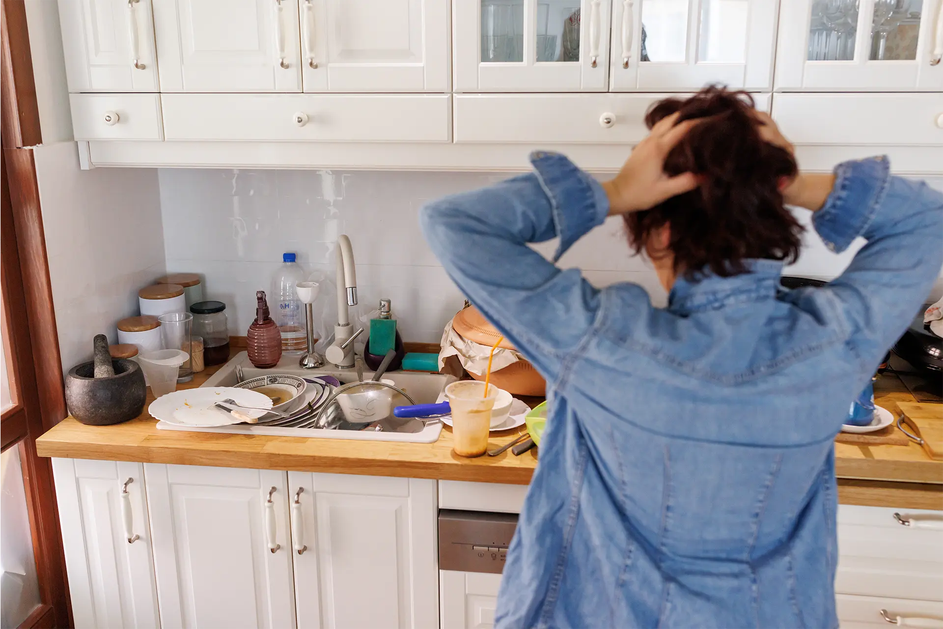 A woman in a mess kitchen grabbing her hair in frustration