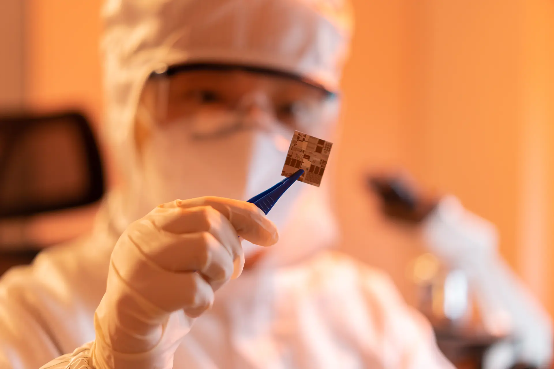 Man in protective clothing holding a silicon chip in tweezers