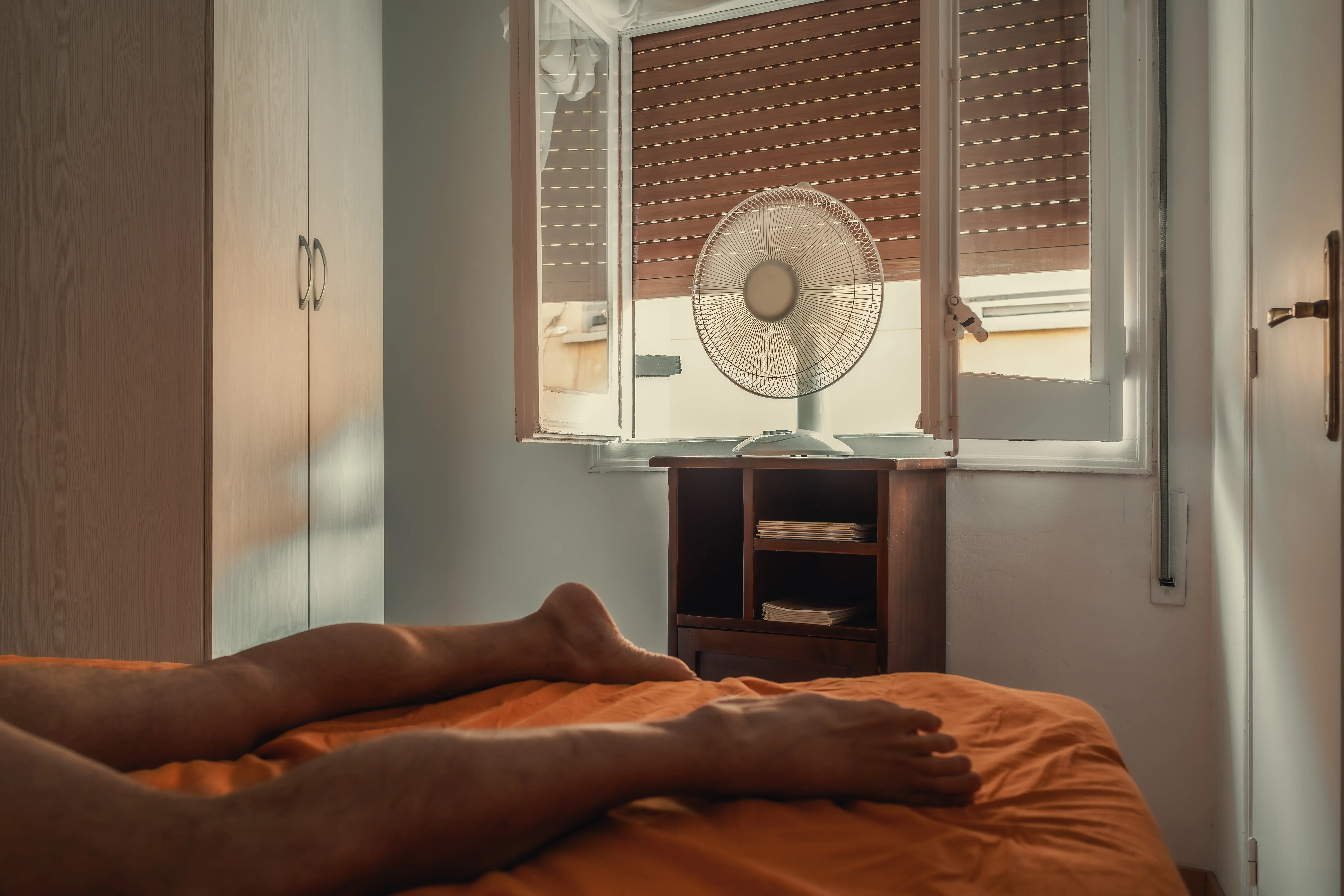 The legs of a man lying in a hot room with a fan on