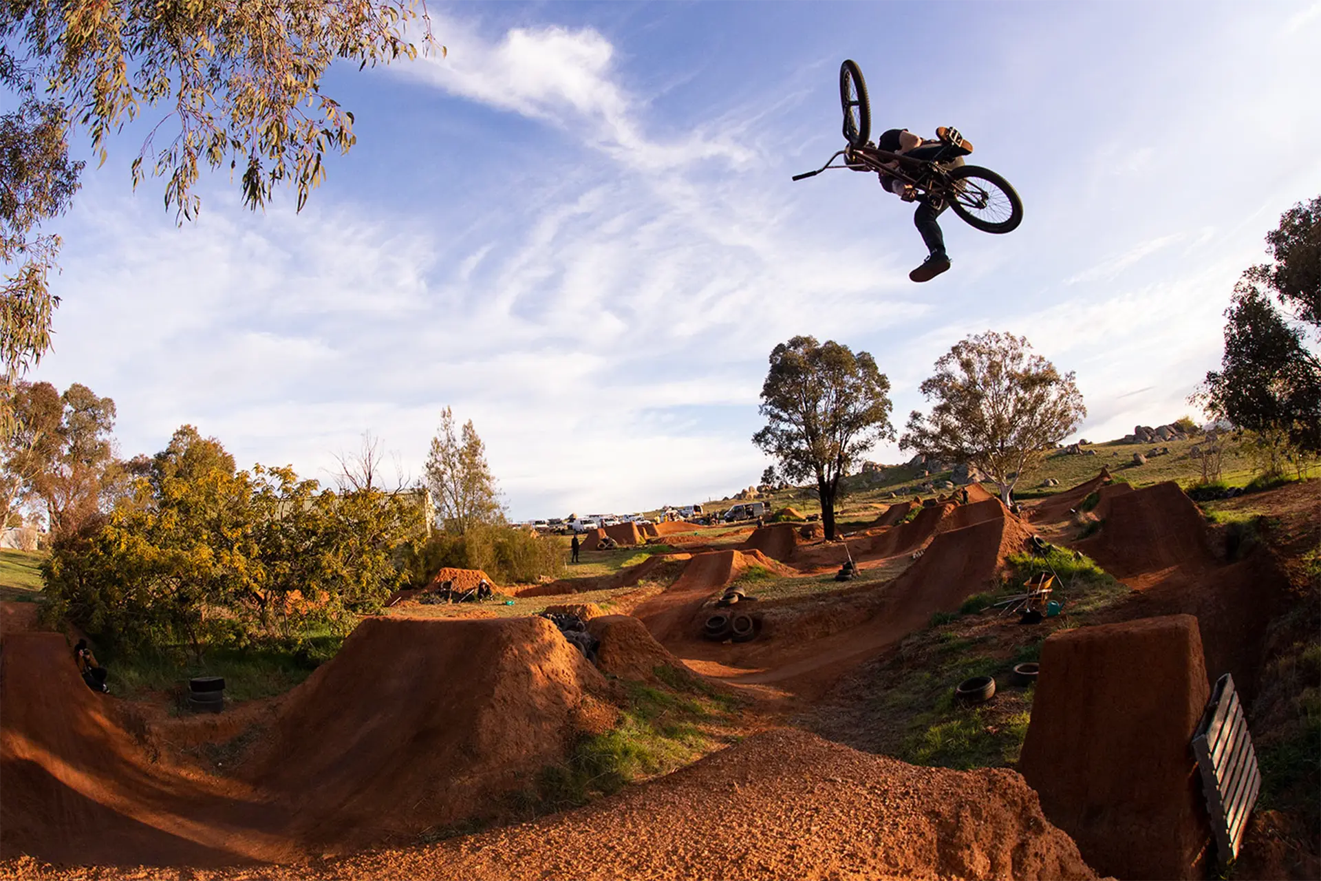 A man on a BMX in mid-jump off in a dirt jumps track