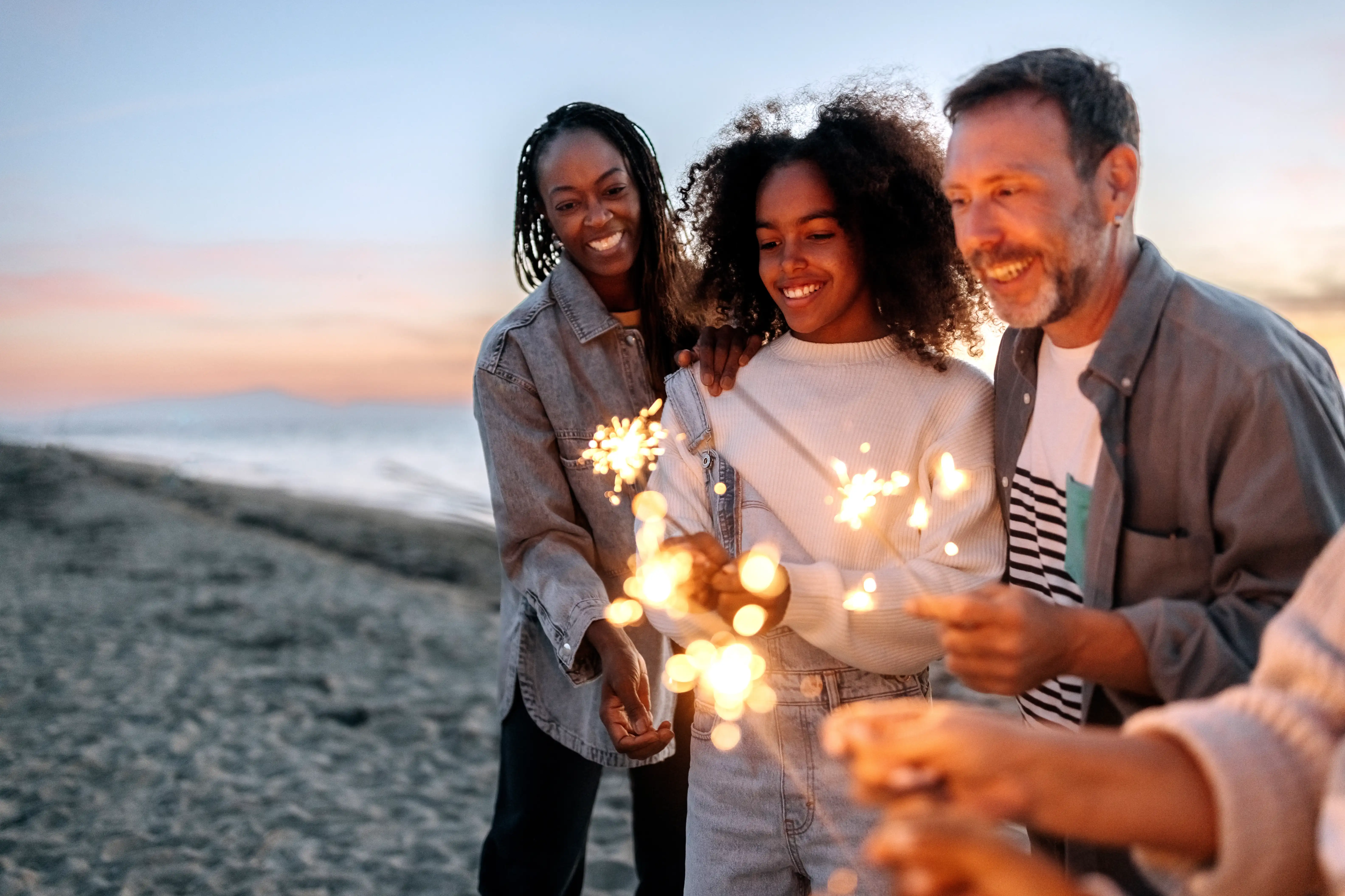 A mother, father and their daughter play with sparklers on a beach during New Years