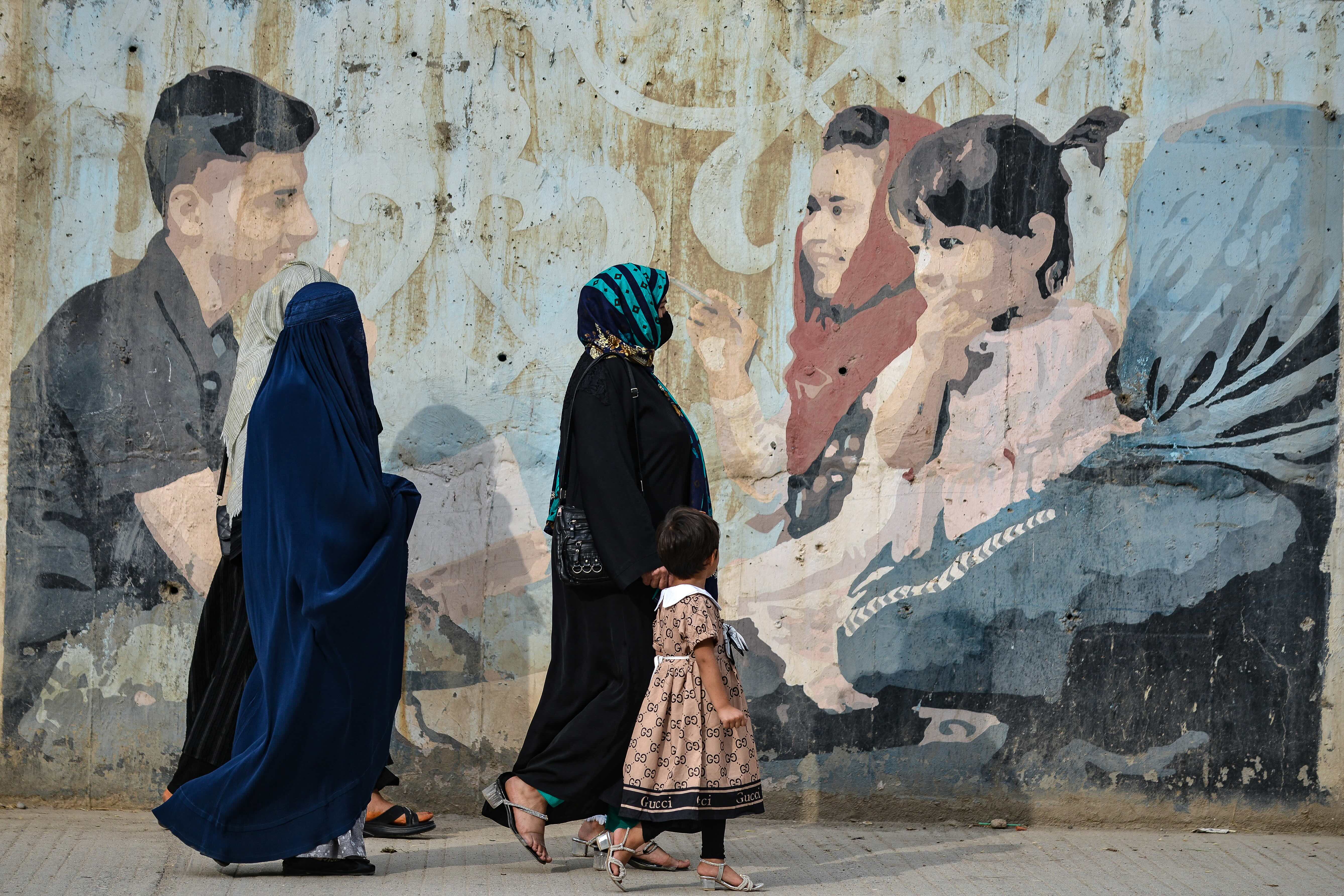 Afghan women walking past mural