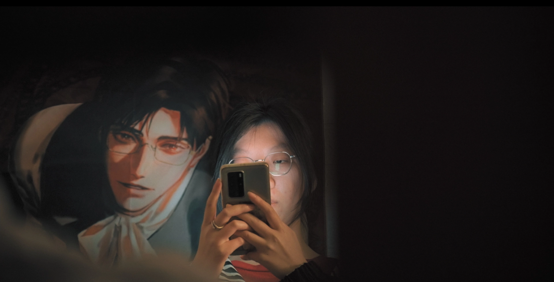 A film still of a woman taking a photo of her and a poster of an anime character