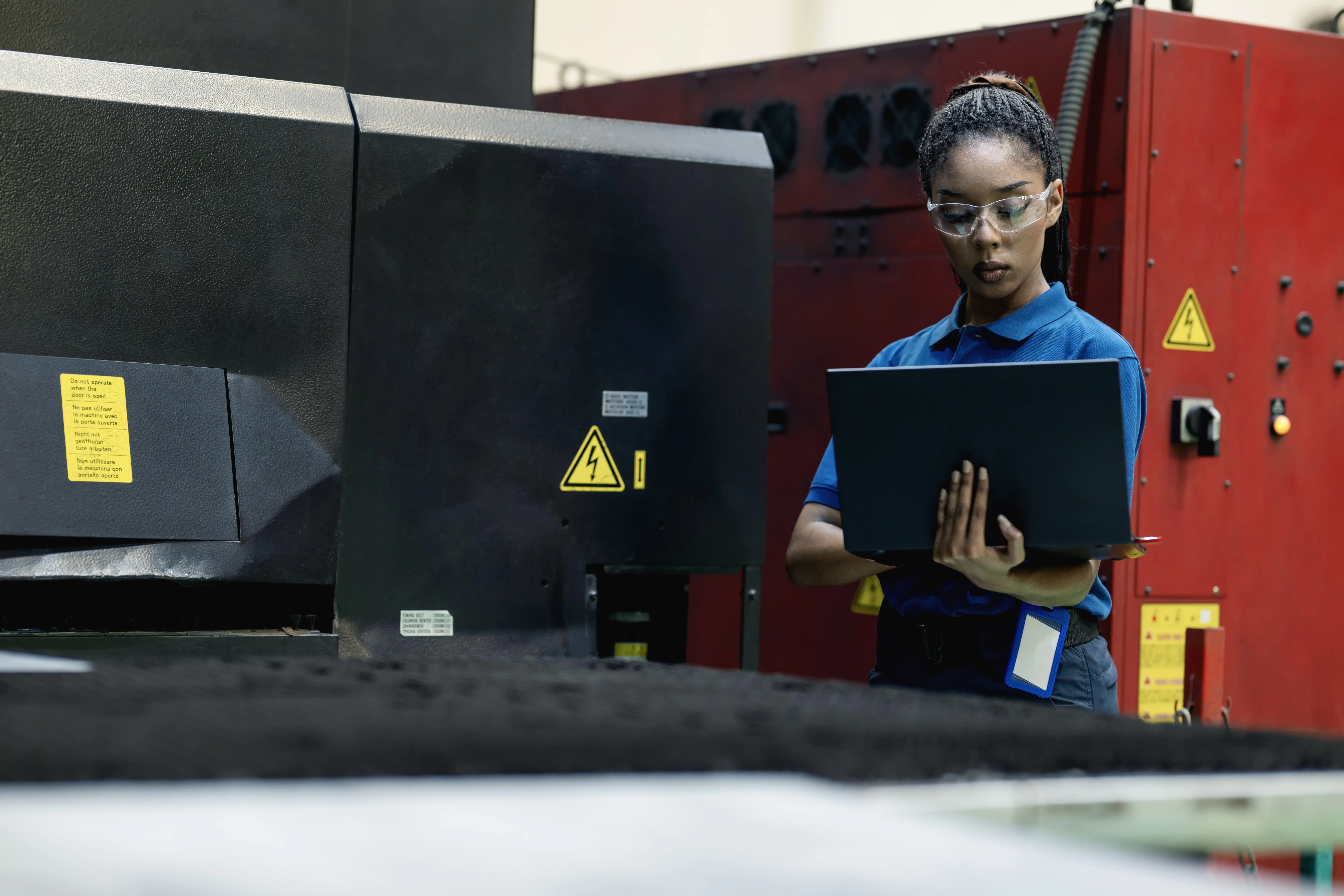 A woman looks at a laptop as she monitors a conveyor belt in a factory