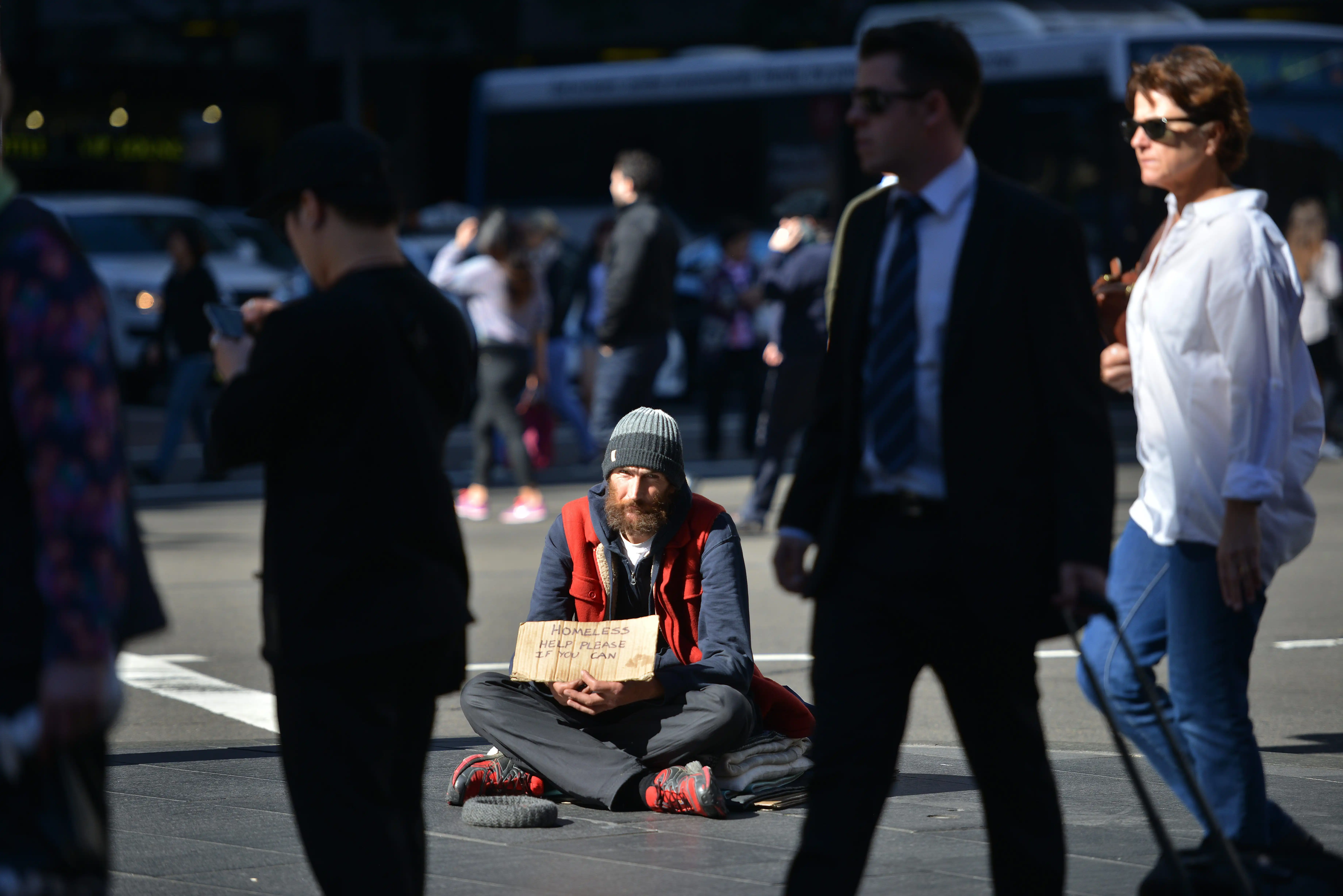 A person who is homeless sits on a street corner with a cardboard sign