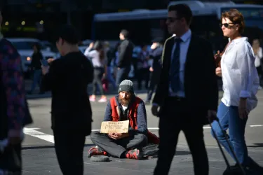 A person who is homeless sits on a street corner with a cardboard sign